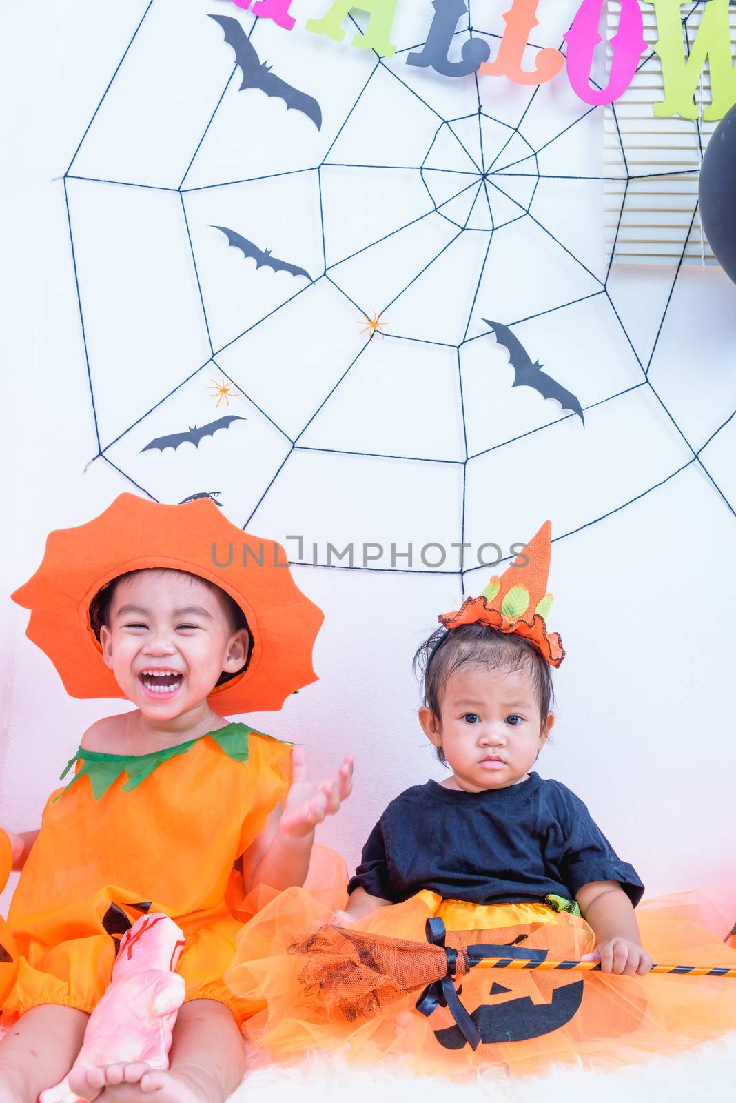 Funny happy brethren baby girl and kid boy in Halloween costume with pumpkin Jack with Cobweb on background
