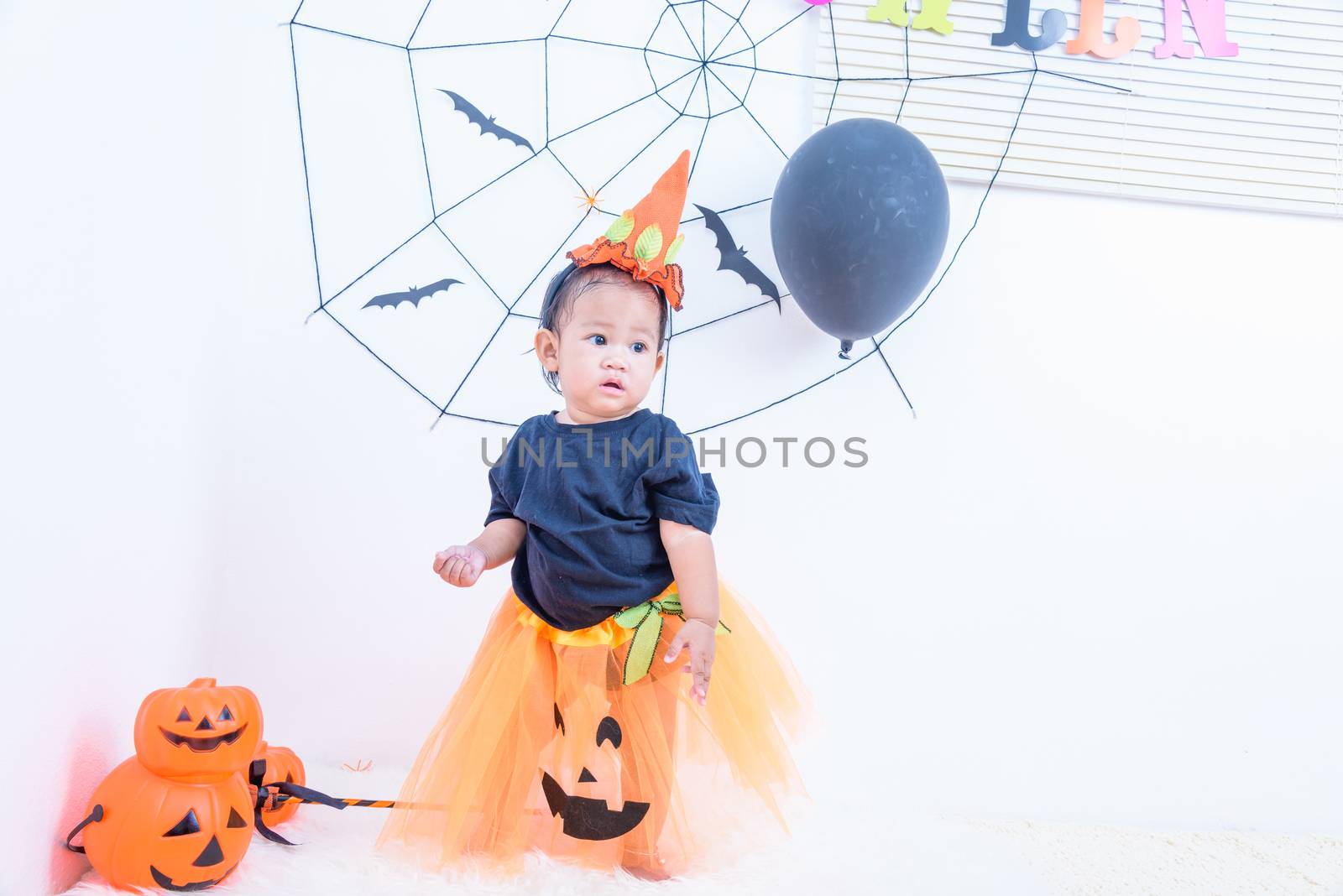 Funny happy baby girl in Halloween costume with pumpkin Jack with Cobweb on background