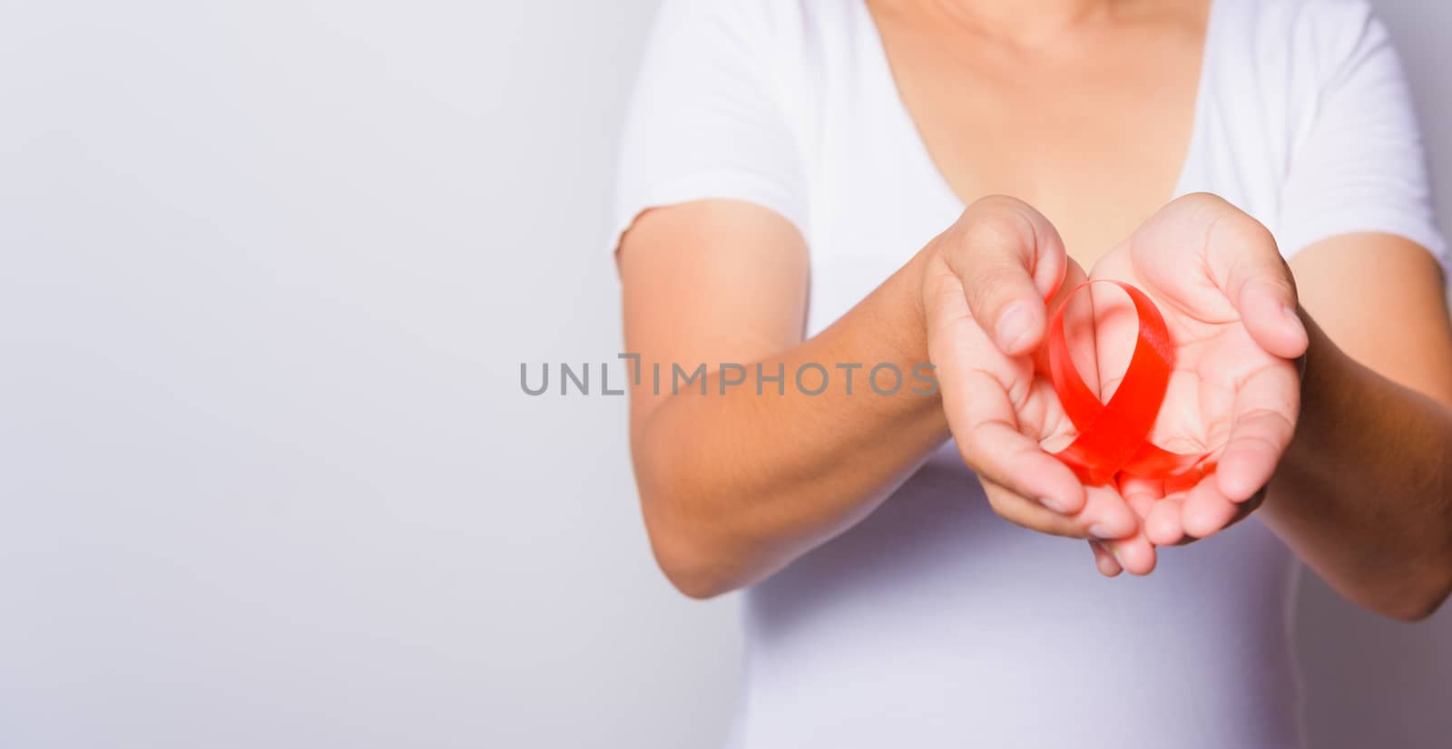 Closeup of female with red ribbon Support HIV AIDS on hands, World AIDS Day and medicine concept with copy space for use