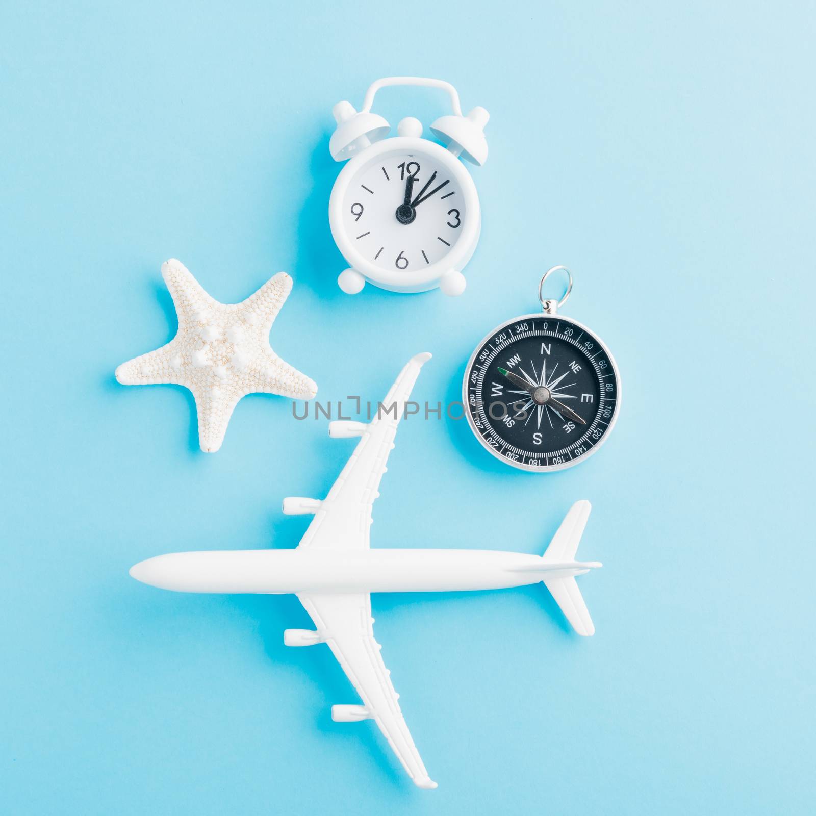 World Tourism Day, Top view flat lay of minimal toy model plane, airplane, starfish, alarm clock and compass, studio shot isolated on a blue background, accessory flight holiday concept
