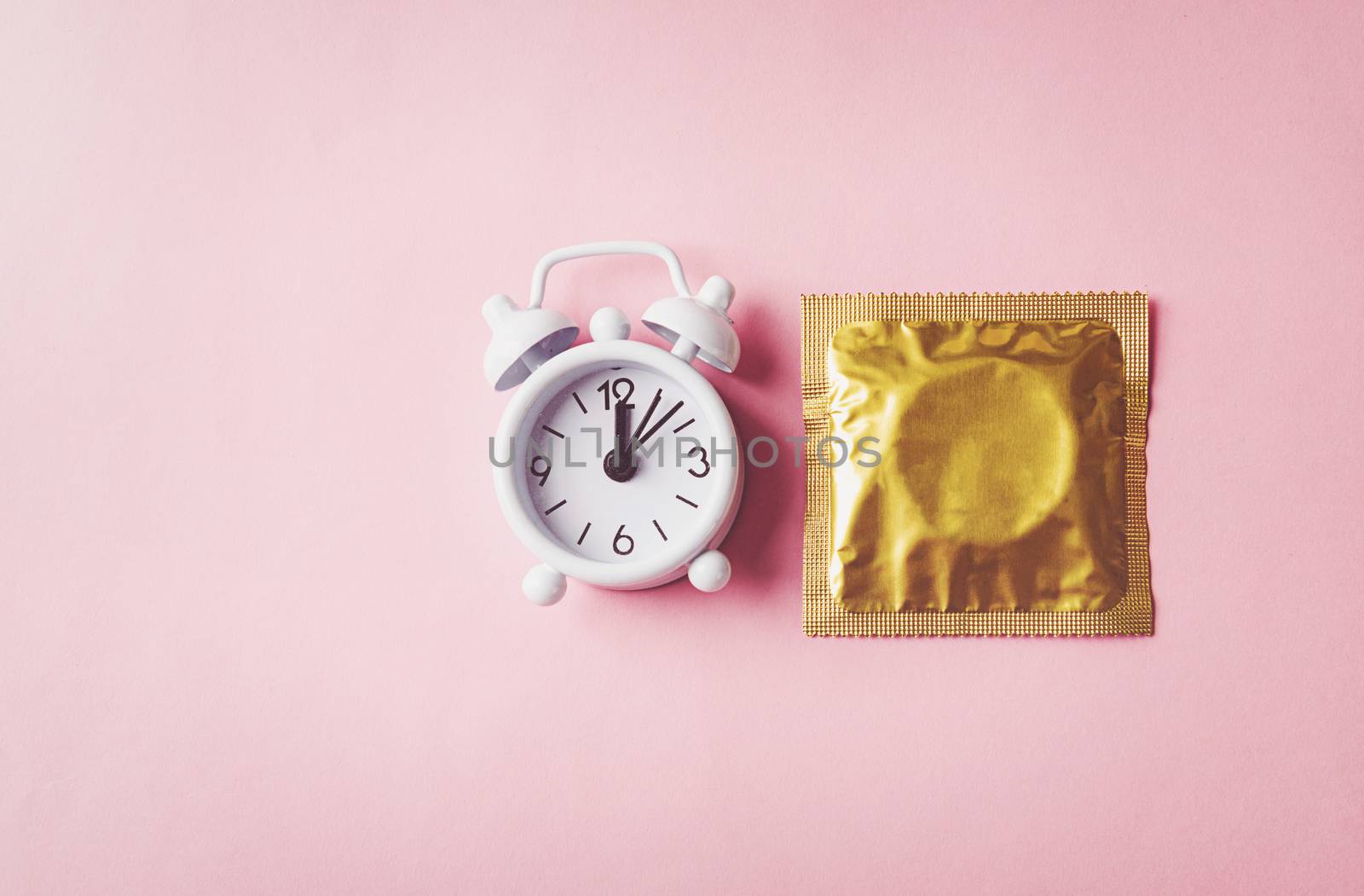 World sexual health or Aids day, condom in wrapper pack and Alarm clock birth control, studio shot isolated on a pink background, Safe sex and reproductive health concept