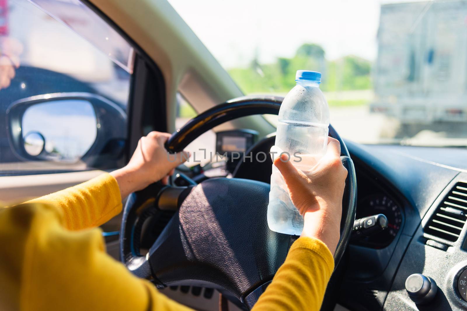 woman holding a water bottle for drink while driving the car by Sorapop