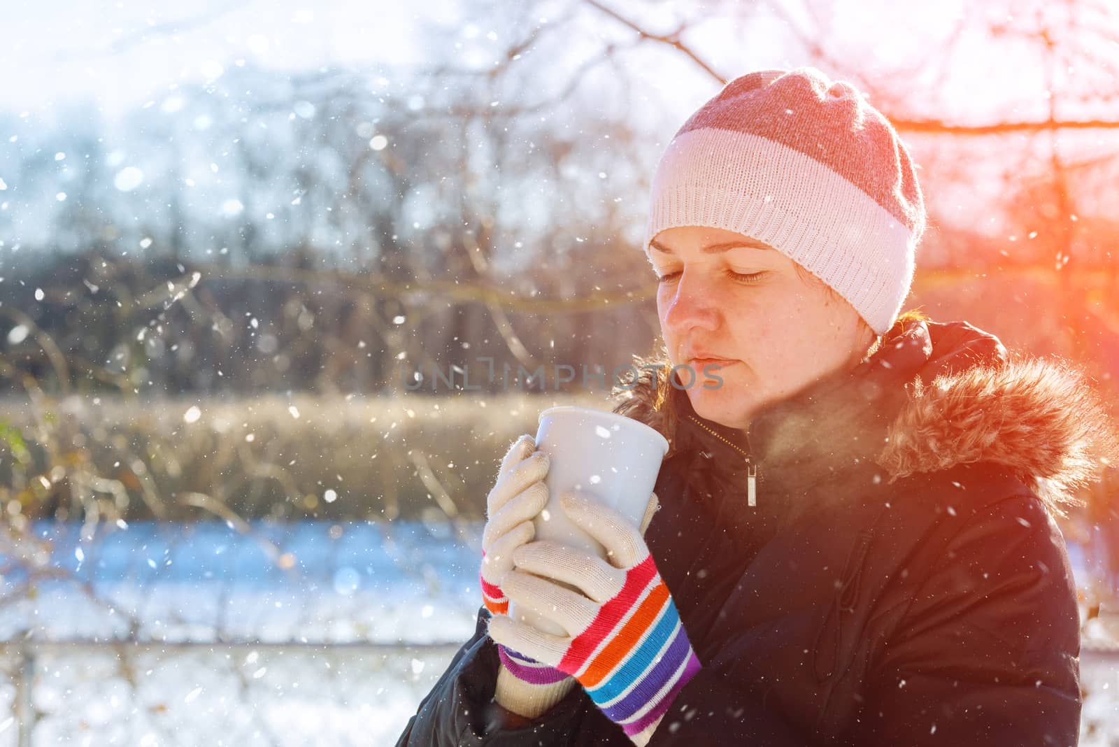 Woman drinking with a mug of hot drink outdoors in winter sunny day