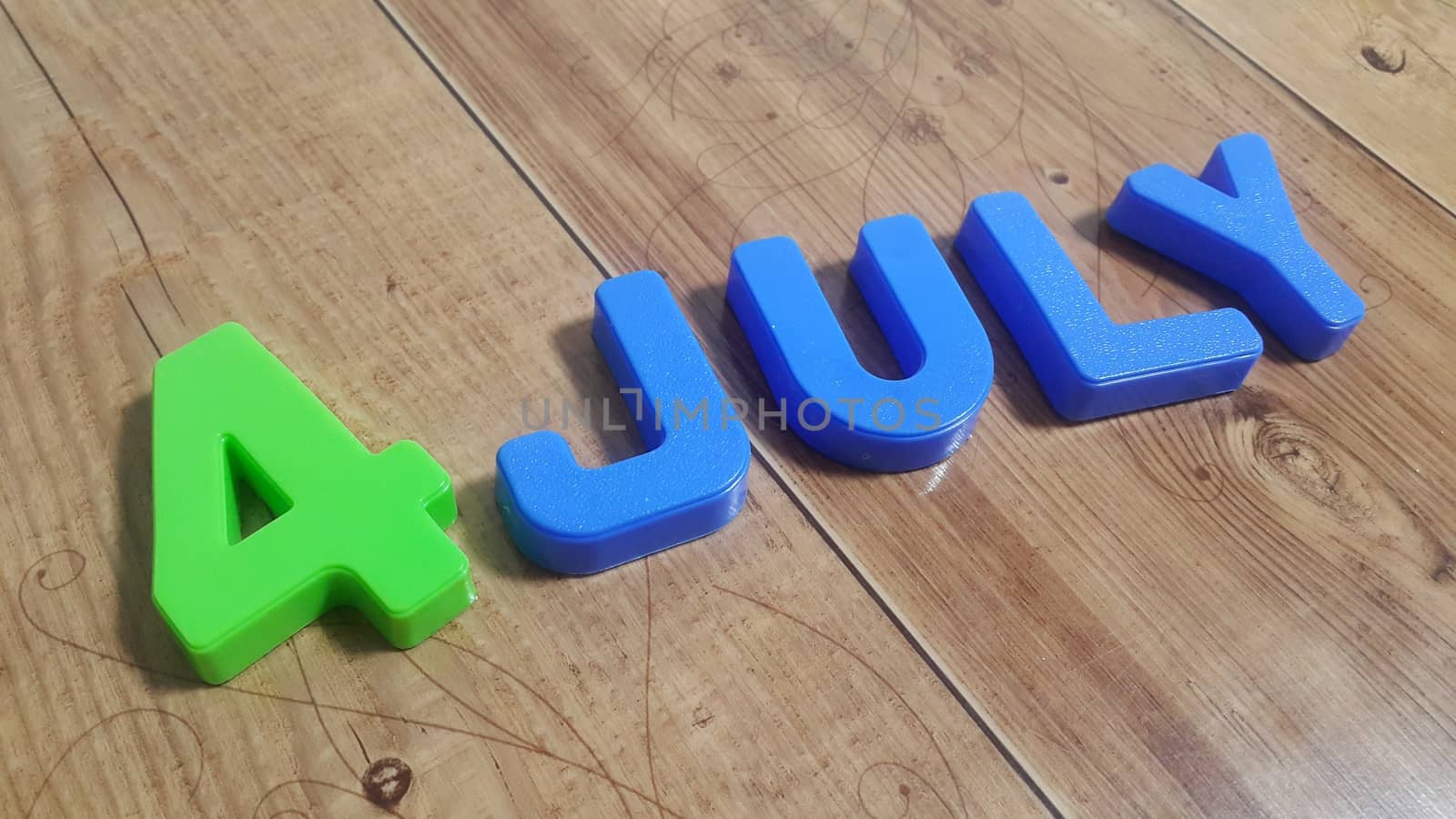 Plastic colored alphabets making words 4 july are placed on a wooden floor. These plastic letters can be used for teaching kids.
