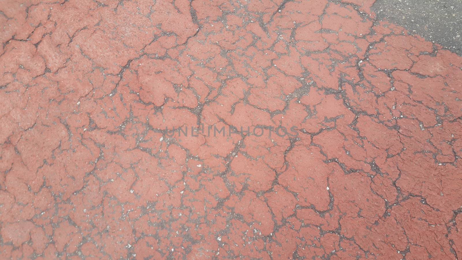 Red colored damaged road or paved pathway with crackes of different shpaes. Cracked texture with copy space for text and messages