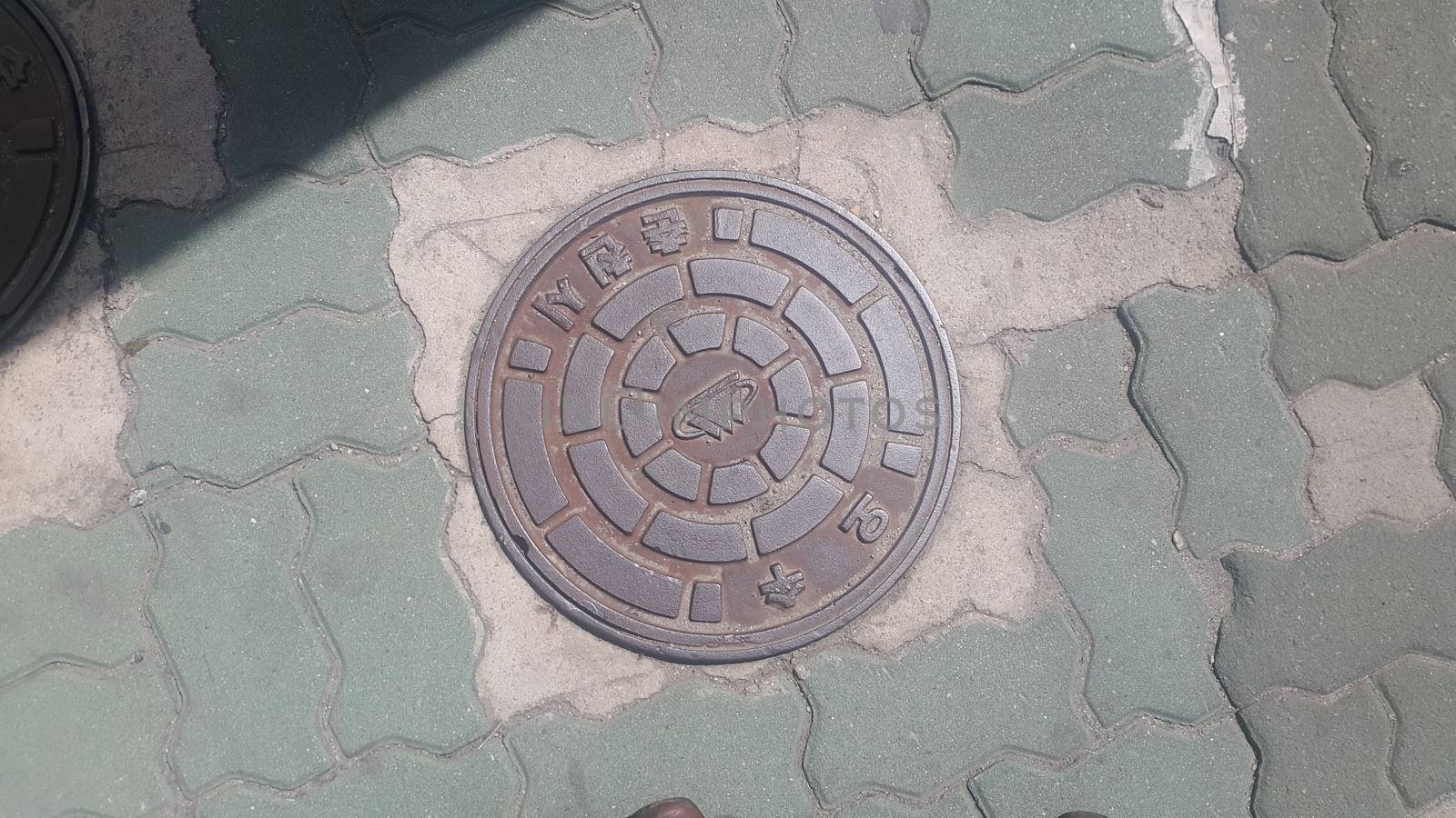 Top view of a manhole cover on drainage or sewerage under paved road. by Photochowk