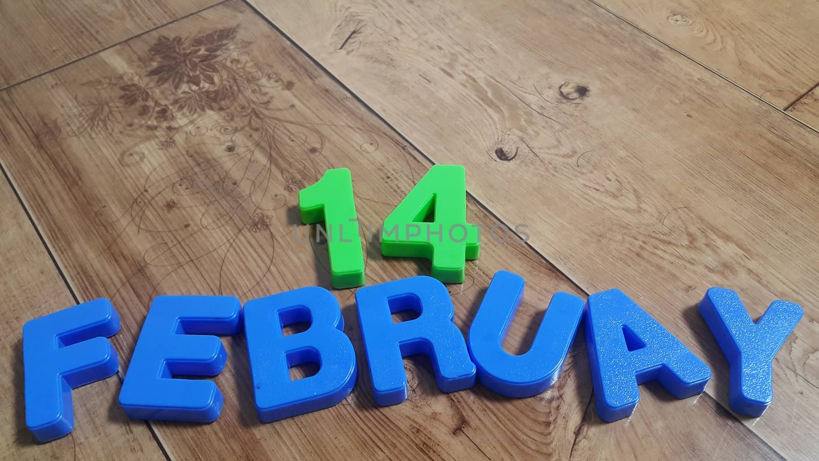 Plastic colored alphabets making words 14 February are placed on a wooden floor. These plastic letters can be used for teaching kids.