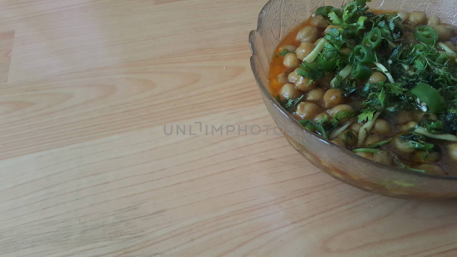 Home made dish served in glass bowl garnished with sliced onion and green coriander leaf and placed over wooden floor .Traditional lentils Channa Masala or chickpeas curry or chole bhature.