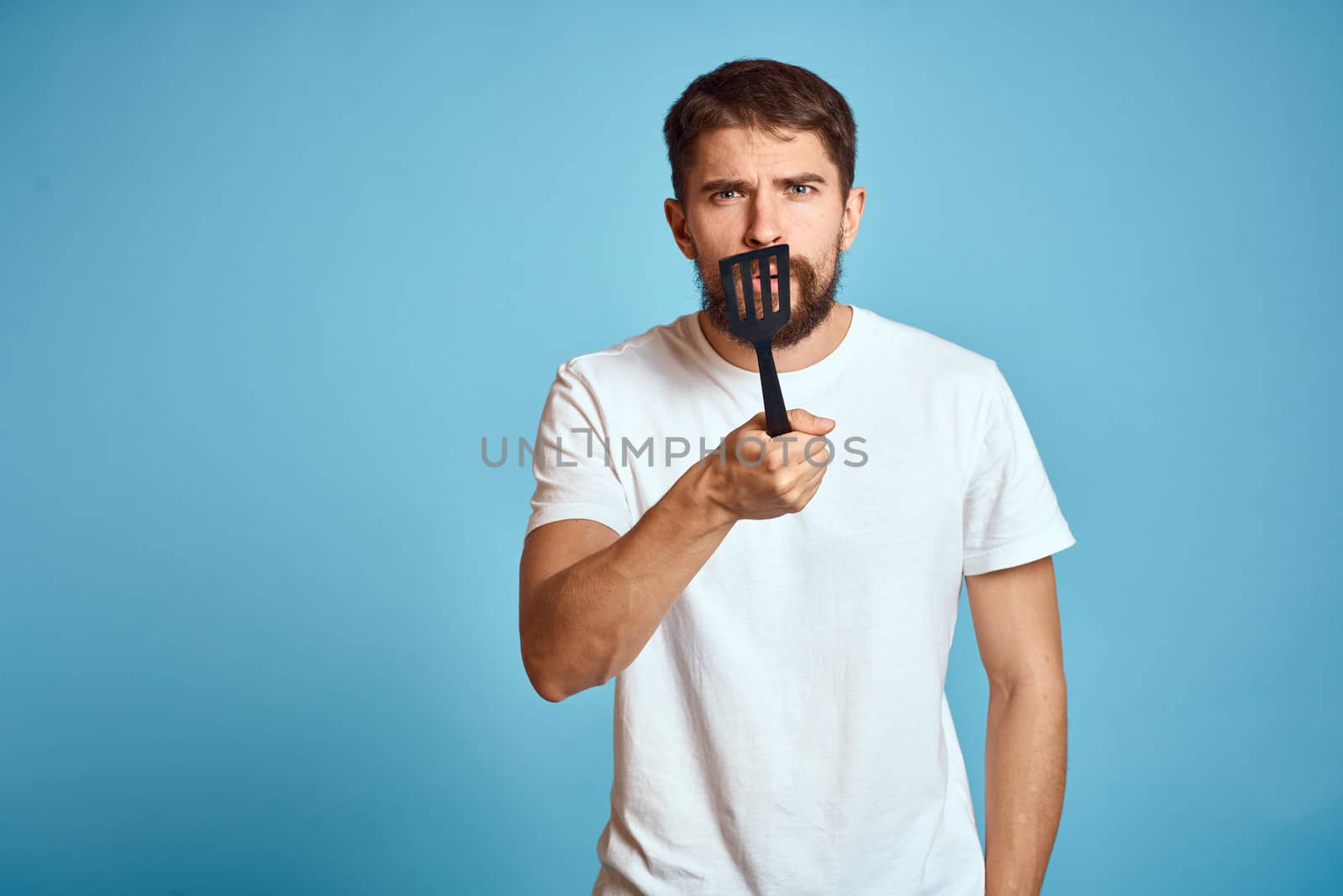 A man with a shovel for cooking in his hand on a blue background and a white T-shirt. High quality photo