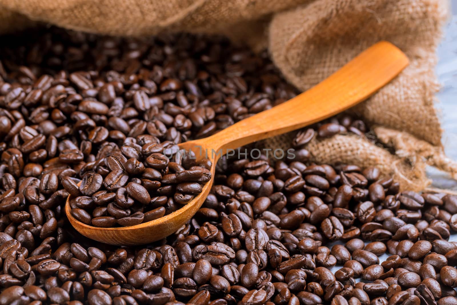 Black coffee beans in bag with wooden spoon.