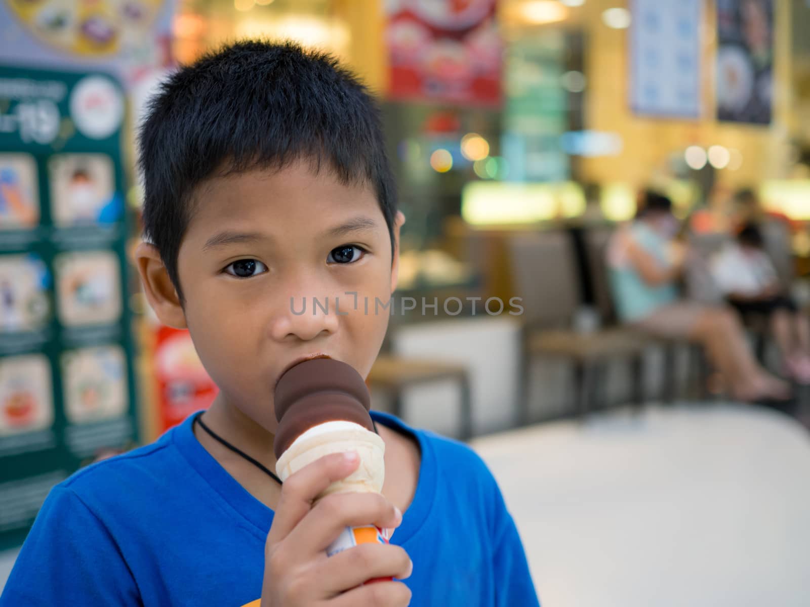 A boy eating ice cream inside a mall with a blurred background. by Unimages2527