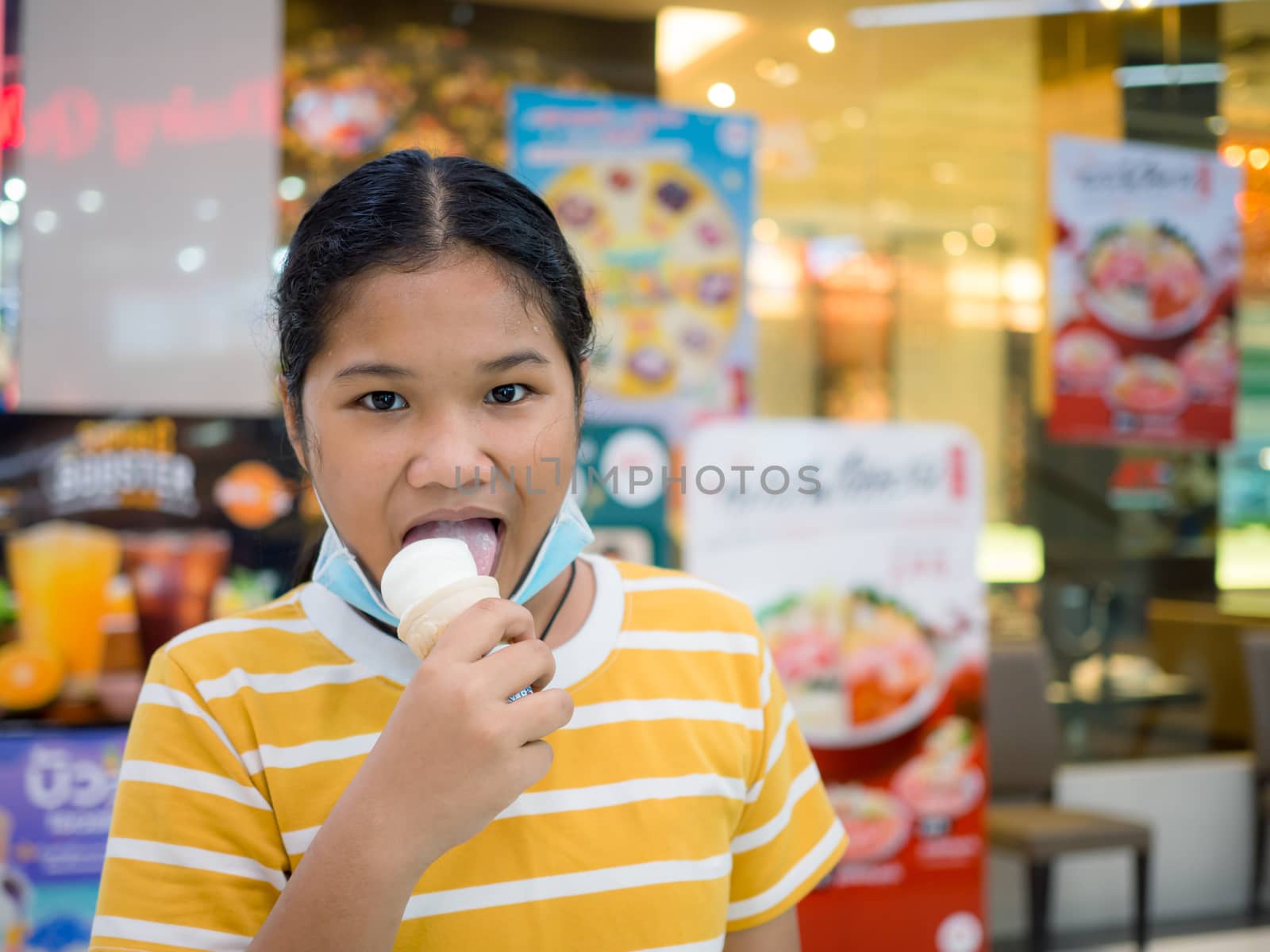 Little girl eating ice cream inside the mall with blurred background.