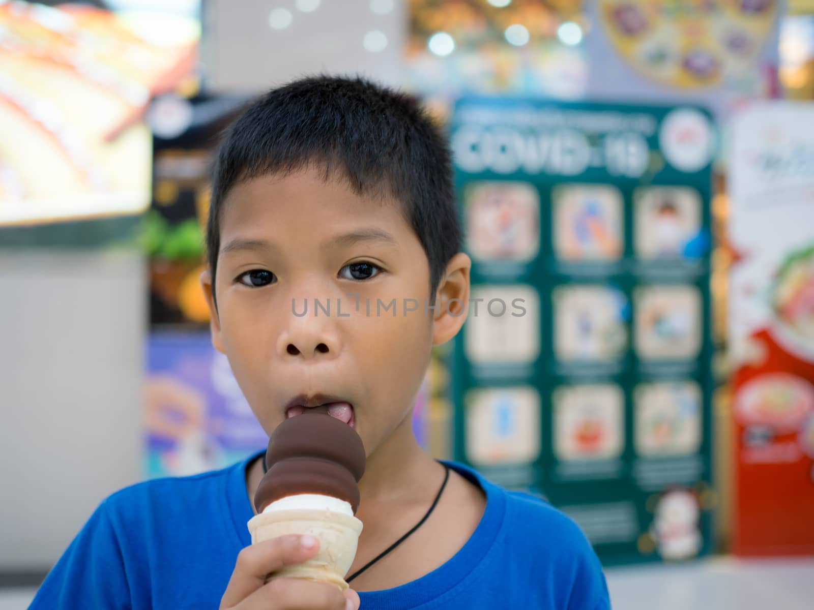 A boy eating ice cream inside a mall with a blurred background.