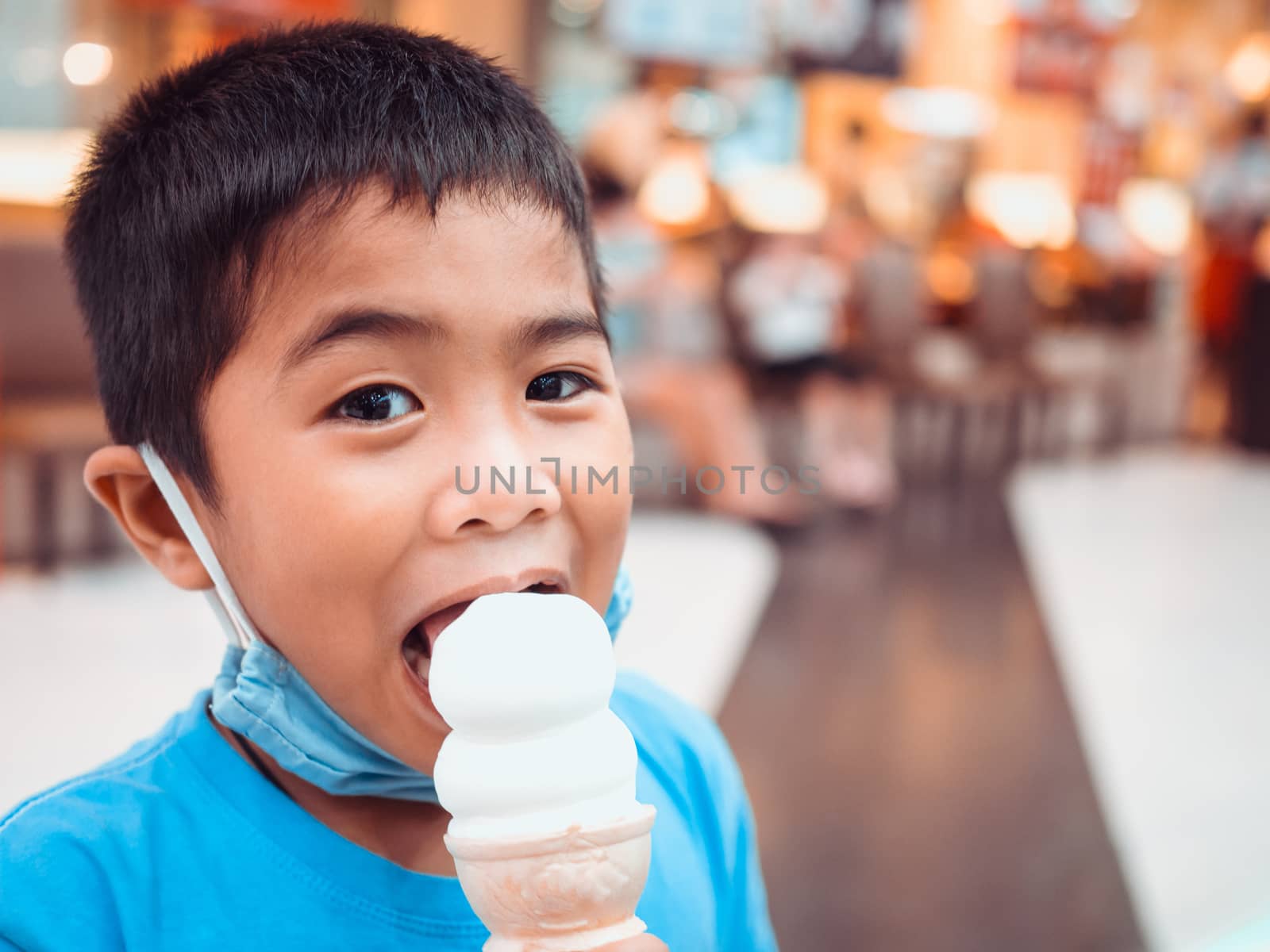 A boy eating ice cream inside a mall with a blurred background
