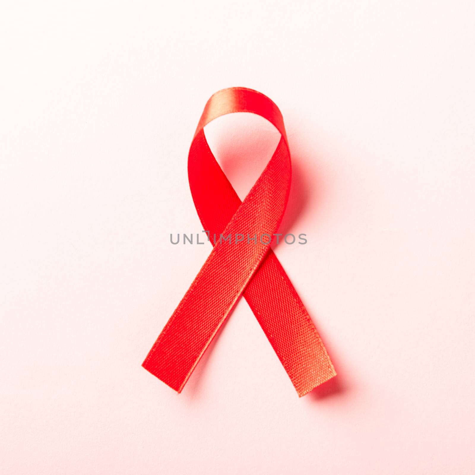 Red bow ribbon symbol HIV, AIDS cancer awareness with shadows, studio shot isolated on pink background, Healthcare medicine concept, World AIDS Day