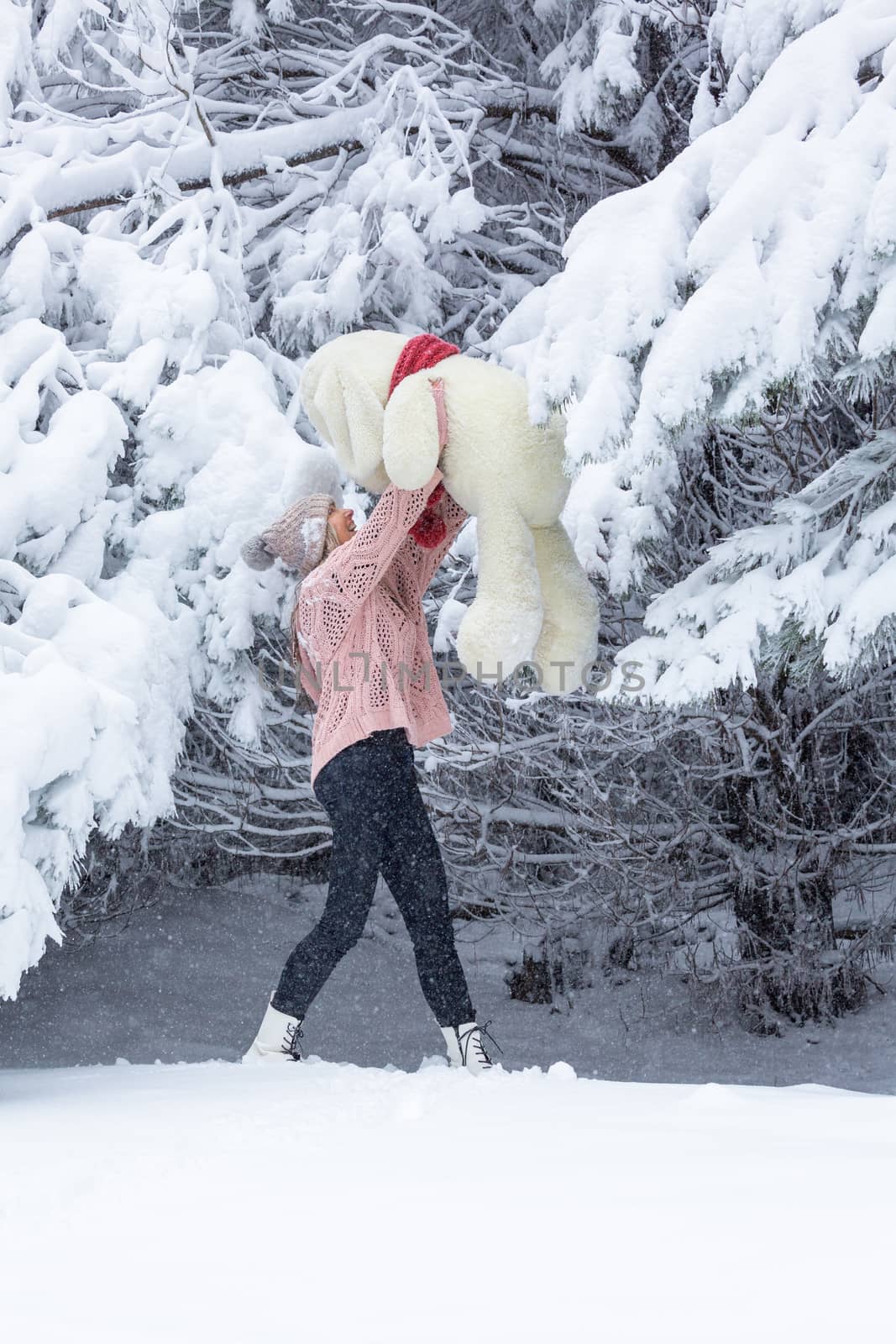 Happy go lucky woman playing in soft fresh snow holding a large soft toy in her arms, high above her head in forest landscape