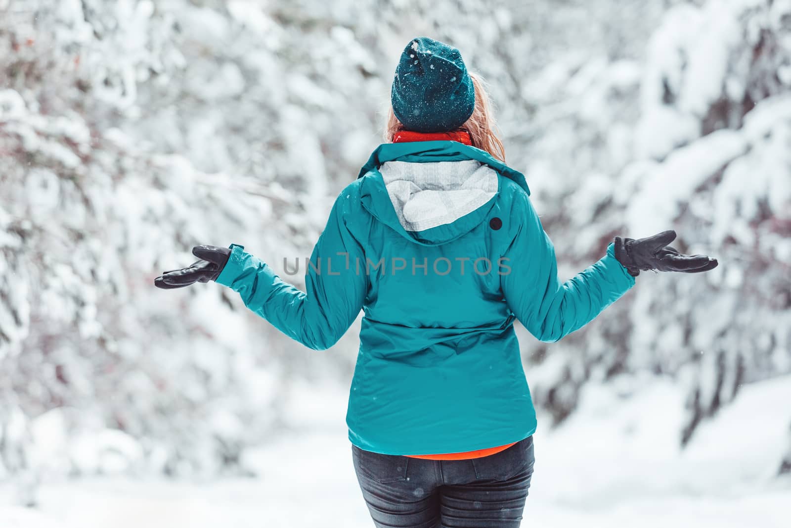 Woman standing in snow among pine forest with snow falling all around her.