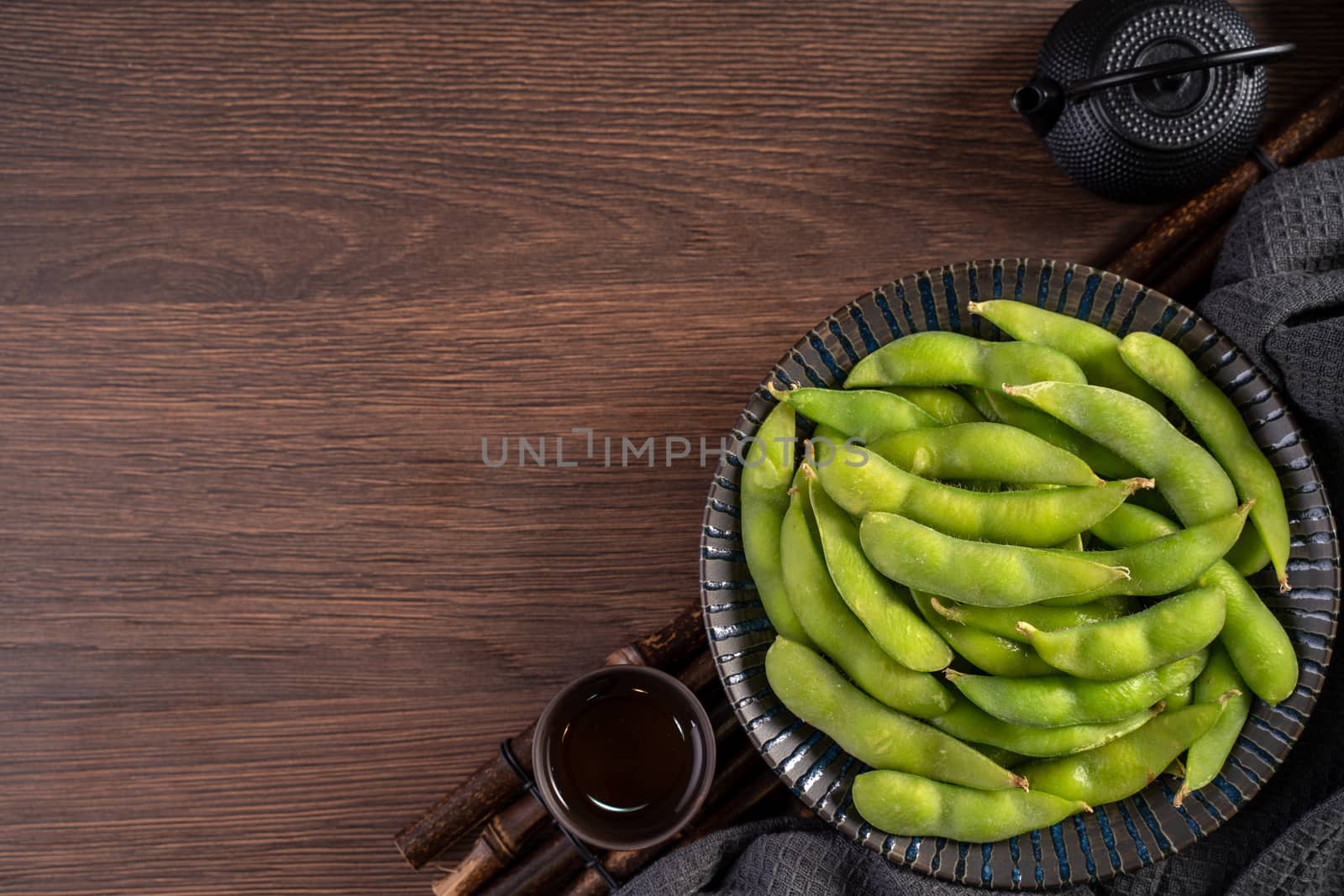 Top view of fresh cooked boiled edamame in a plate on wooden tray and table background with copy space, healthy protein food concept.