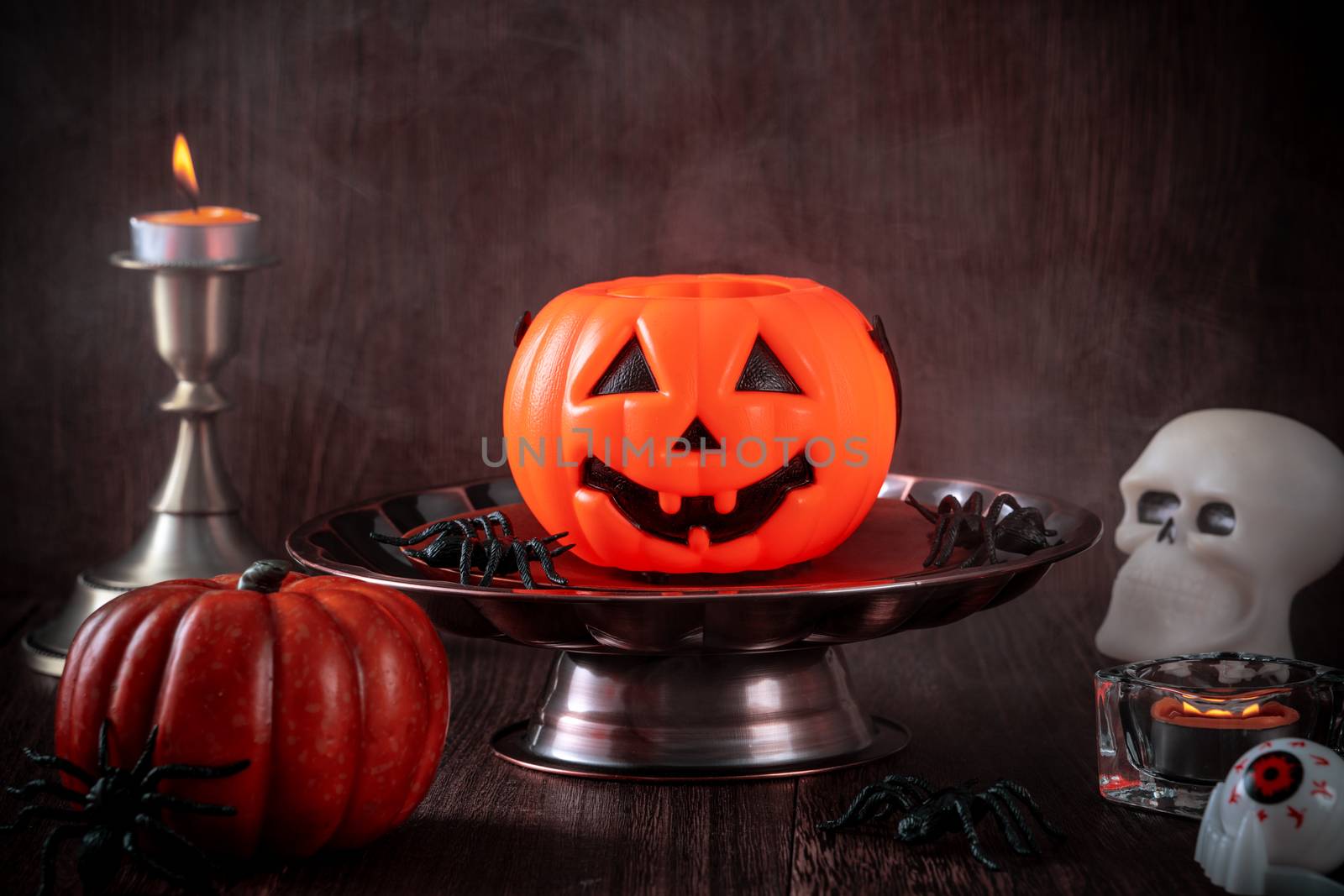 Close up of spooky Halloween tricks, concept of horror festival decor, pumpkin lantern with candlestick and smoke.