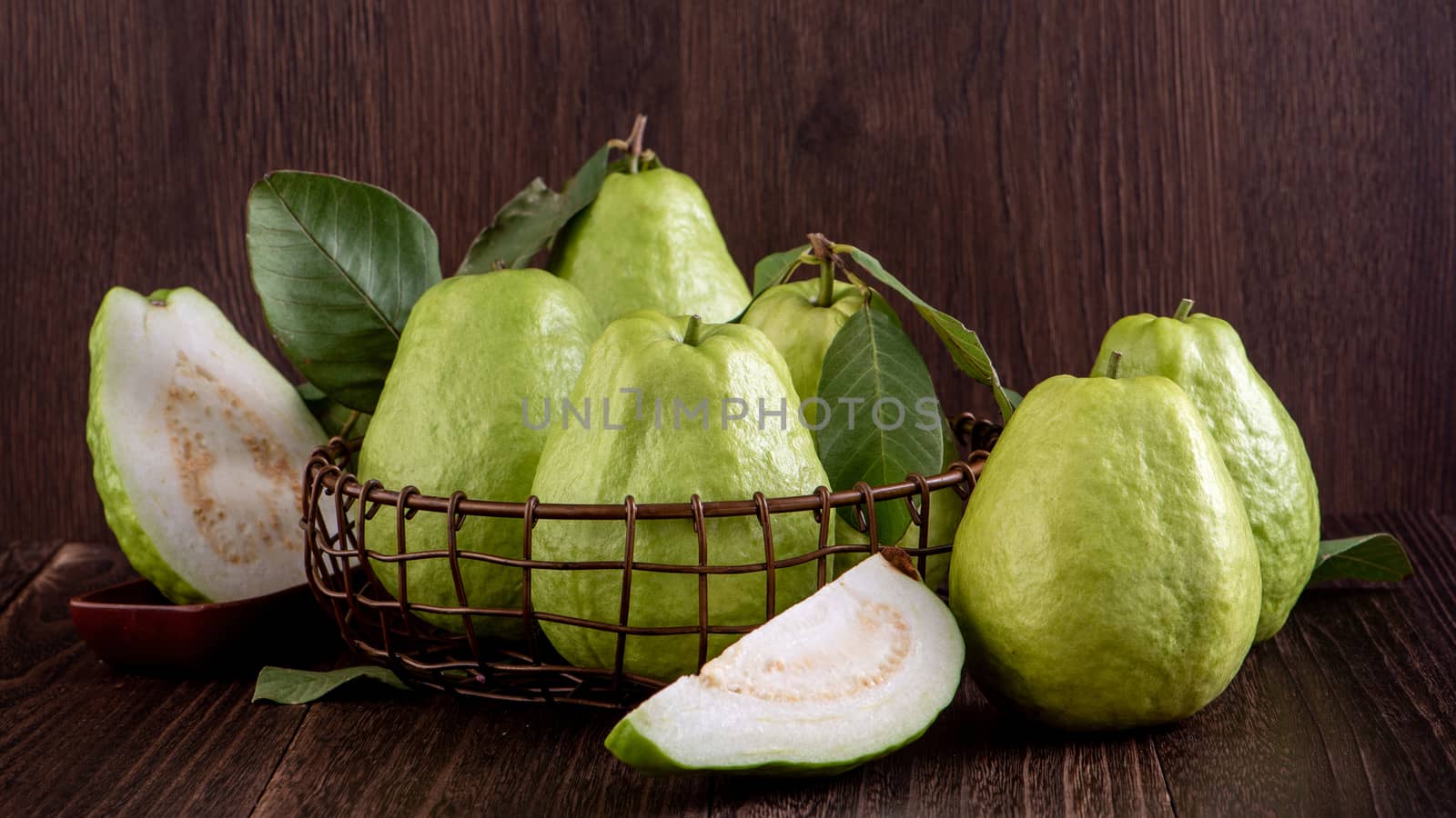 Close up of delicious beautiful guava set with fresh green leaves isolated on dark wooden table background.
