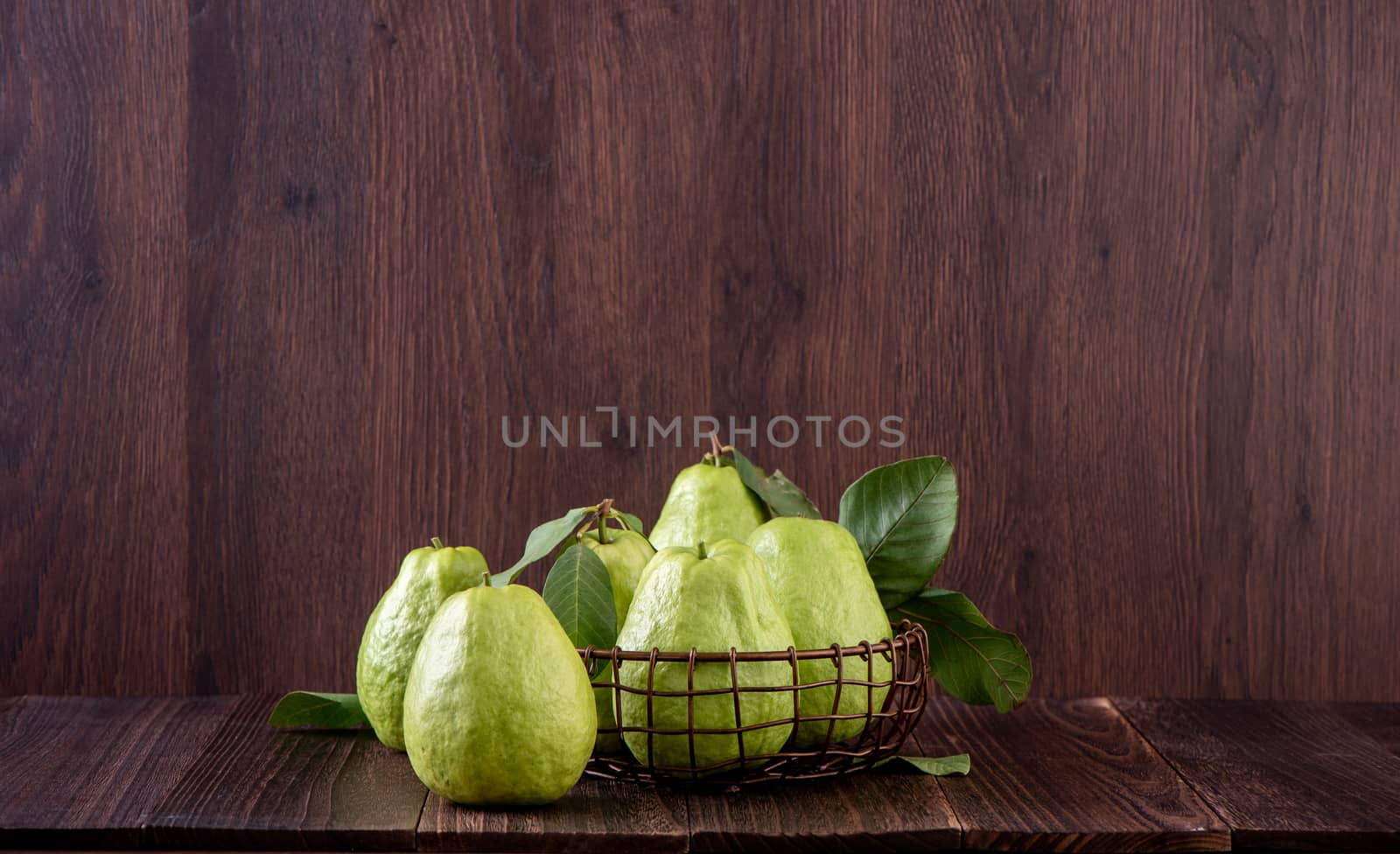 Close up of delicious beautiful guava set with fresh green leaves isolated on dark wooden table background.