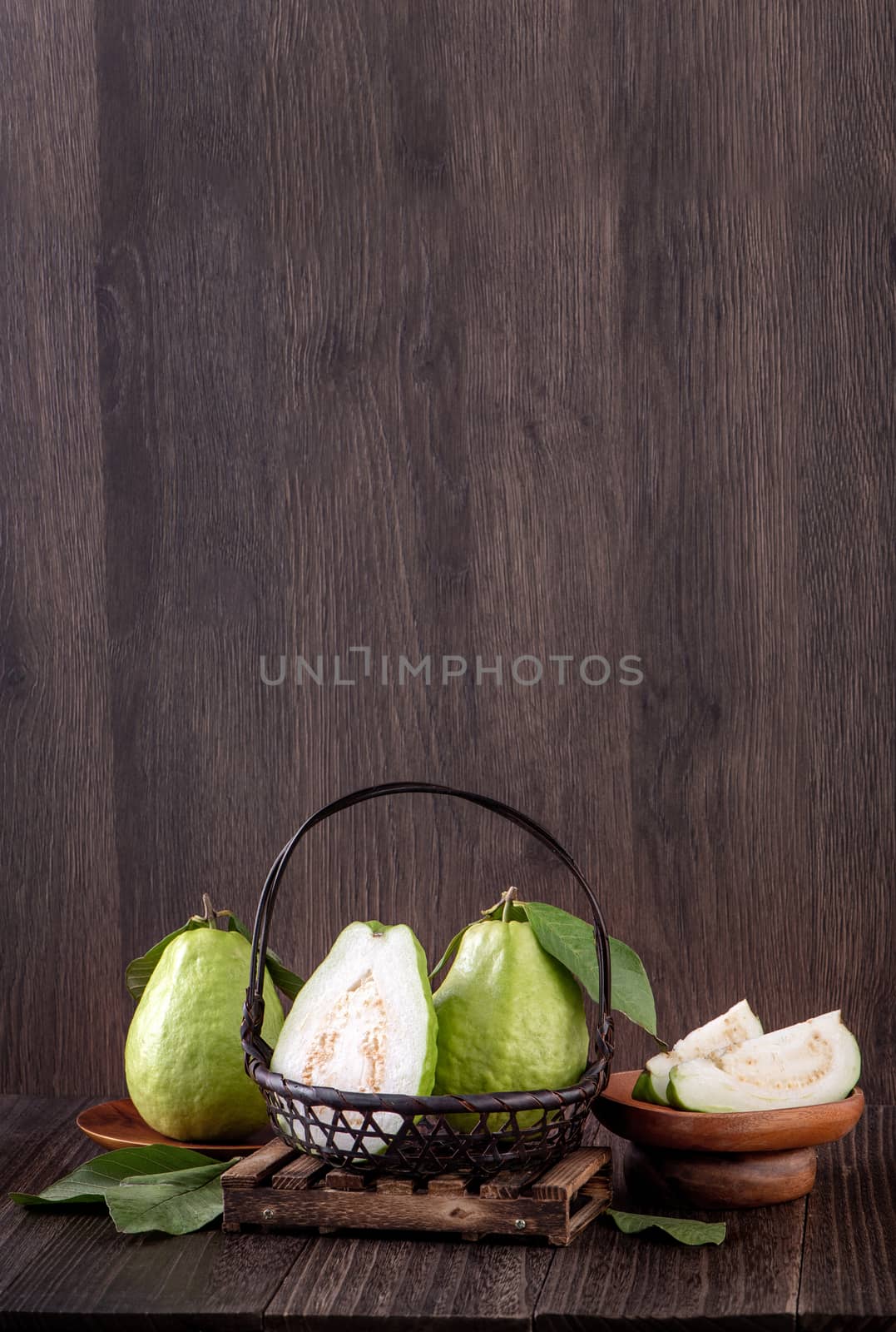 Close up of delicious beautiful guava set with fresh green leaves isolated on dark wooden table background.