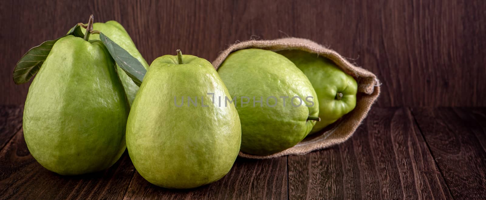 Close up of delicious beautiful guava set with fresh green leaves isolated on dark wooden table background.