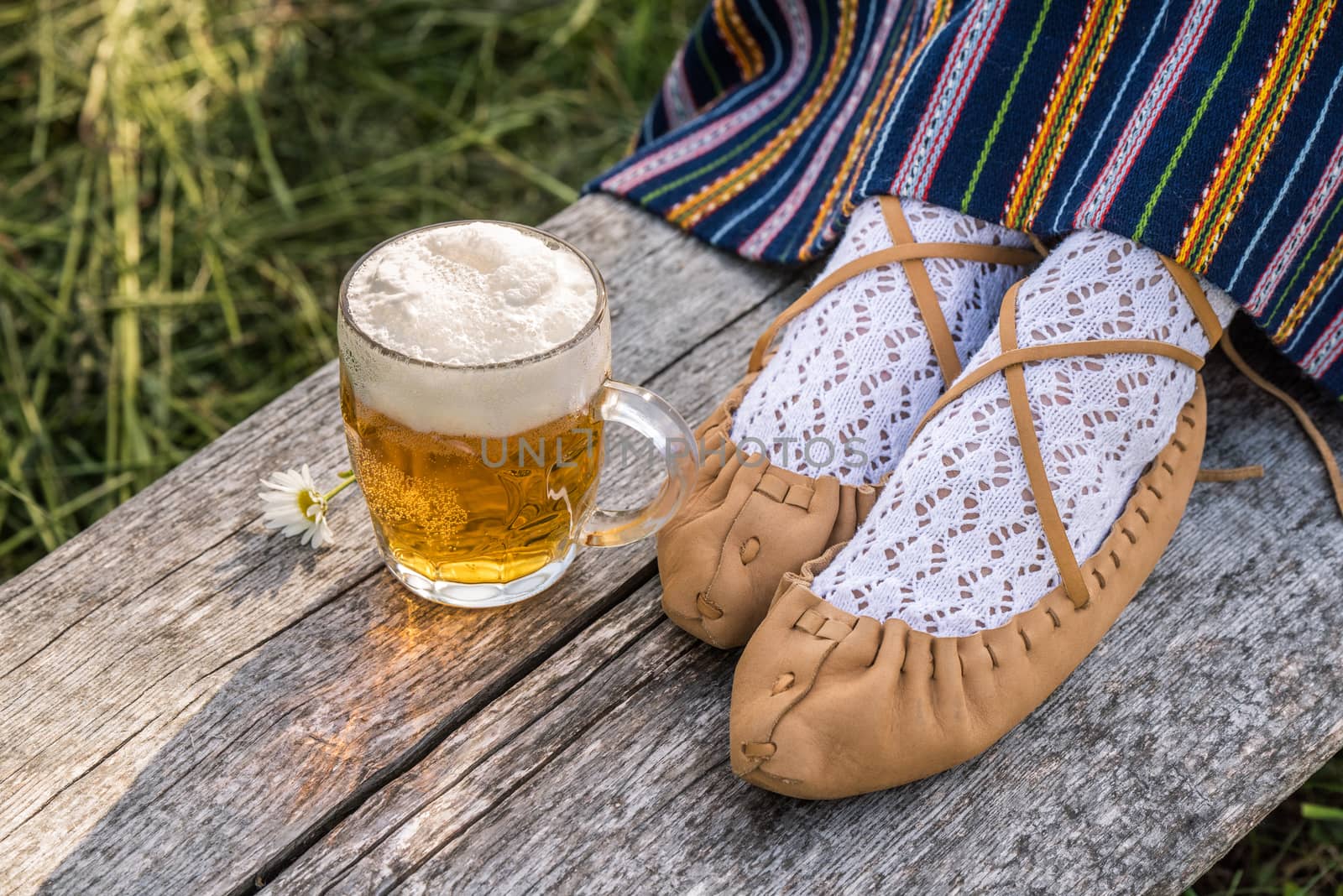 Glass of light beer and leather bast shoes of a Latvian woman in traditional clothing. Preparing Ligo festival. Riga. Latvia