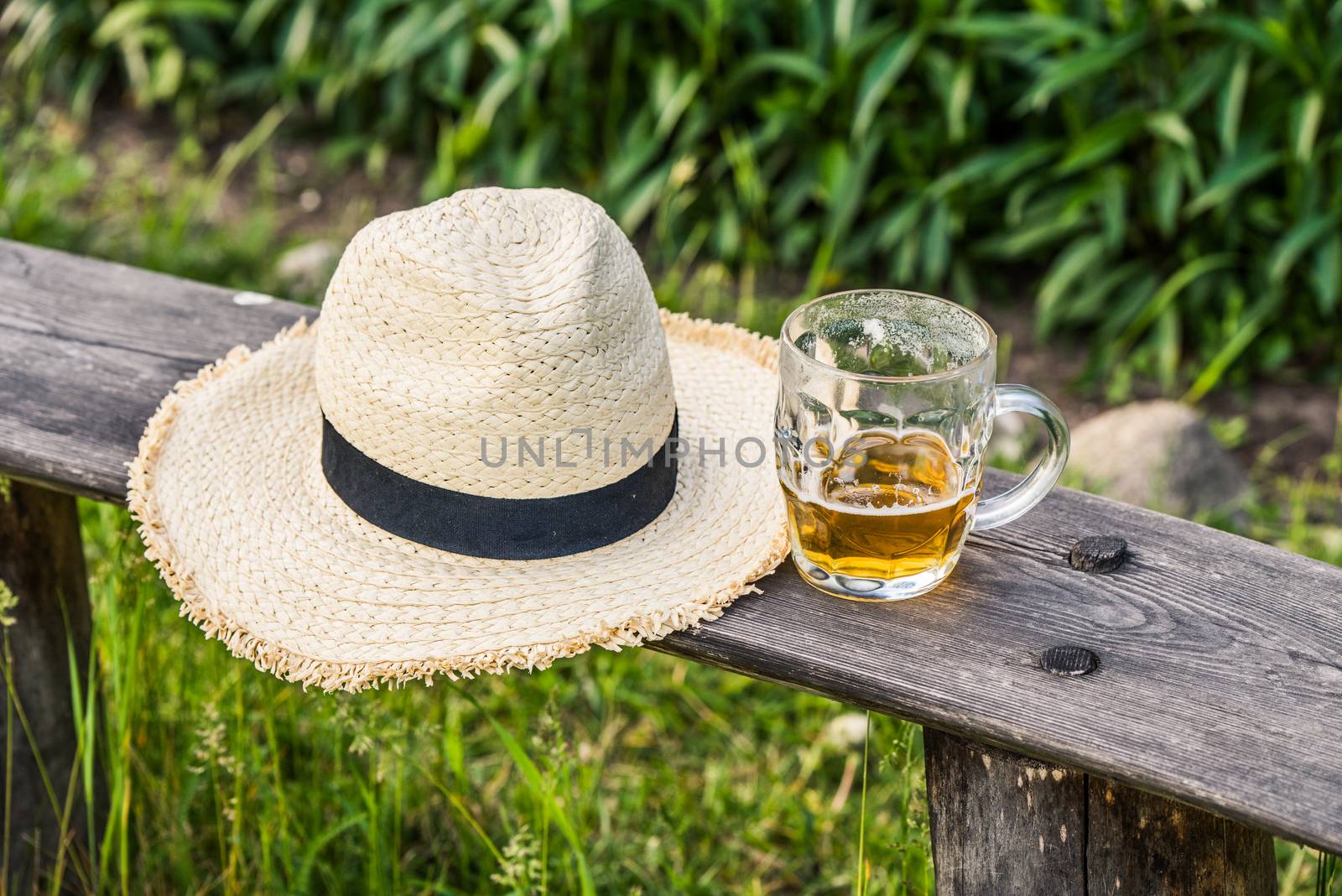 Glass of light beer with a weaving hat on the bench.