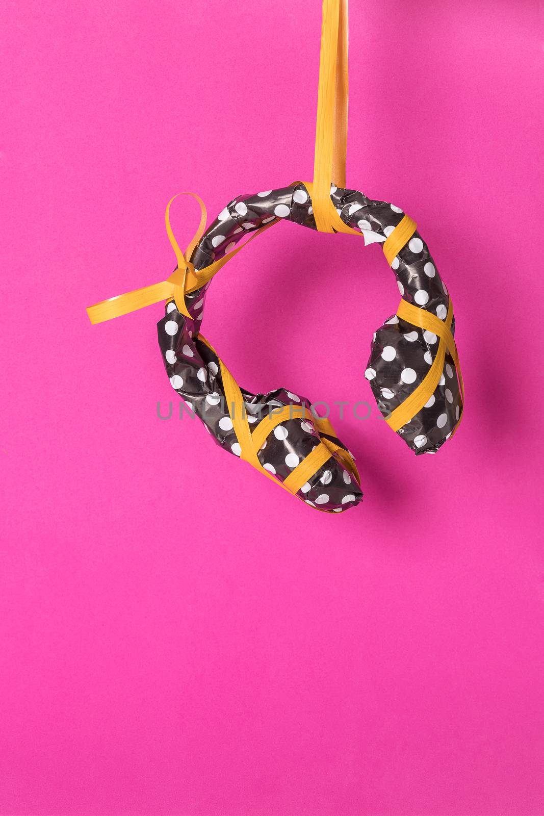 Headphones wrapped in black gift paper with white dots and yellow ribbon on a magenta background