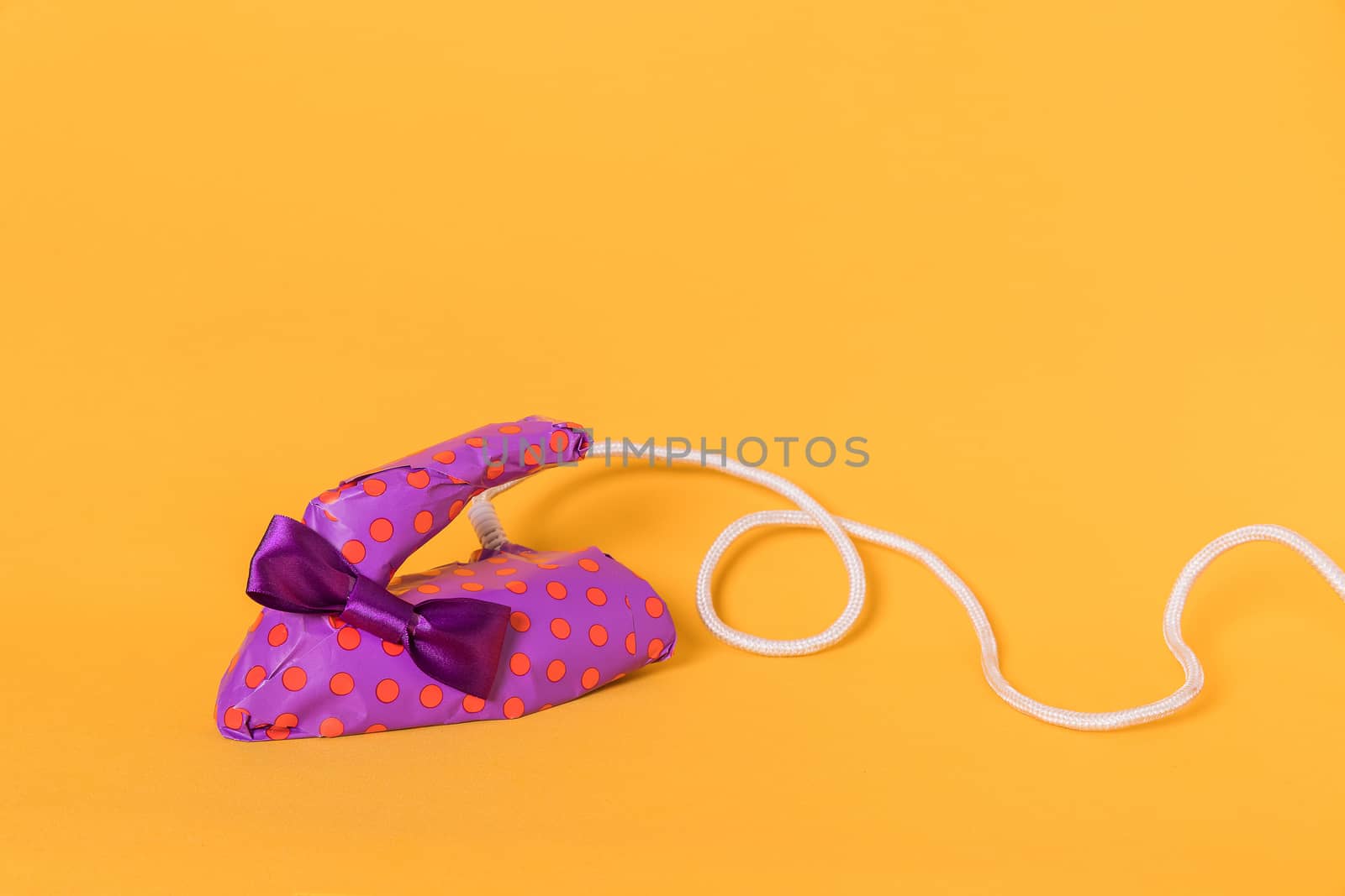 Iron wrapped in purple gift paper on an orange background