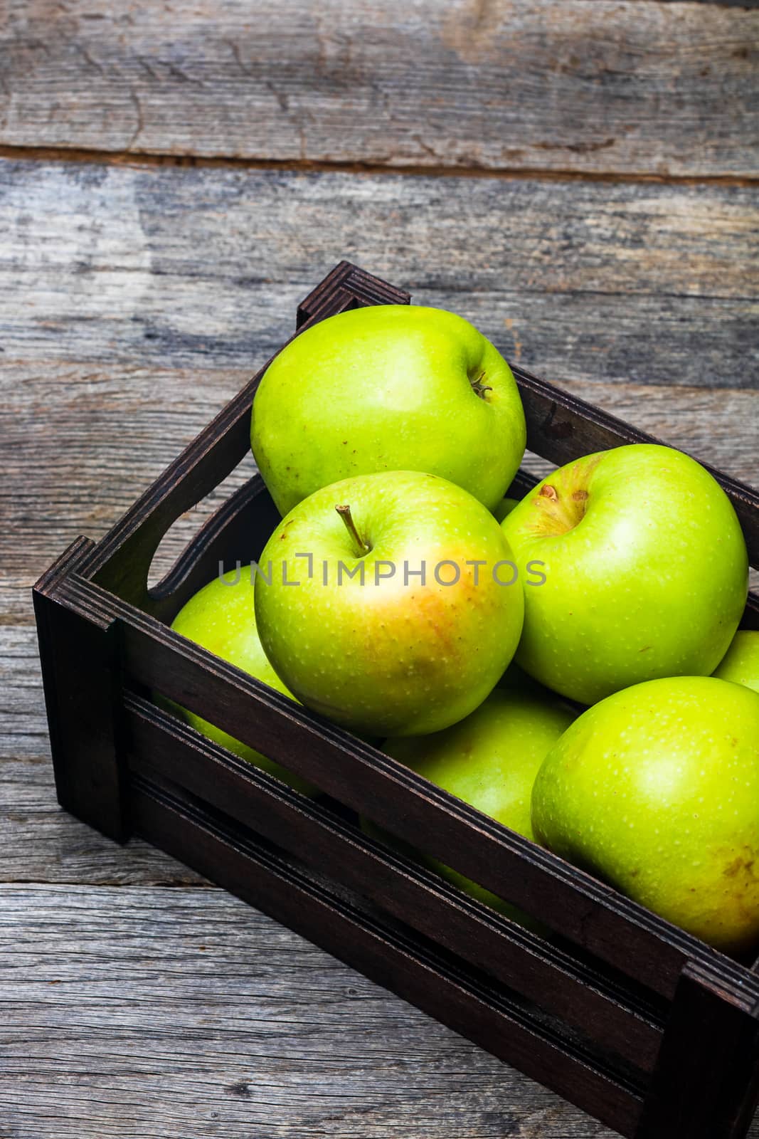 Wooden crate with ripe green apples on wooden table. by vladispas