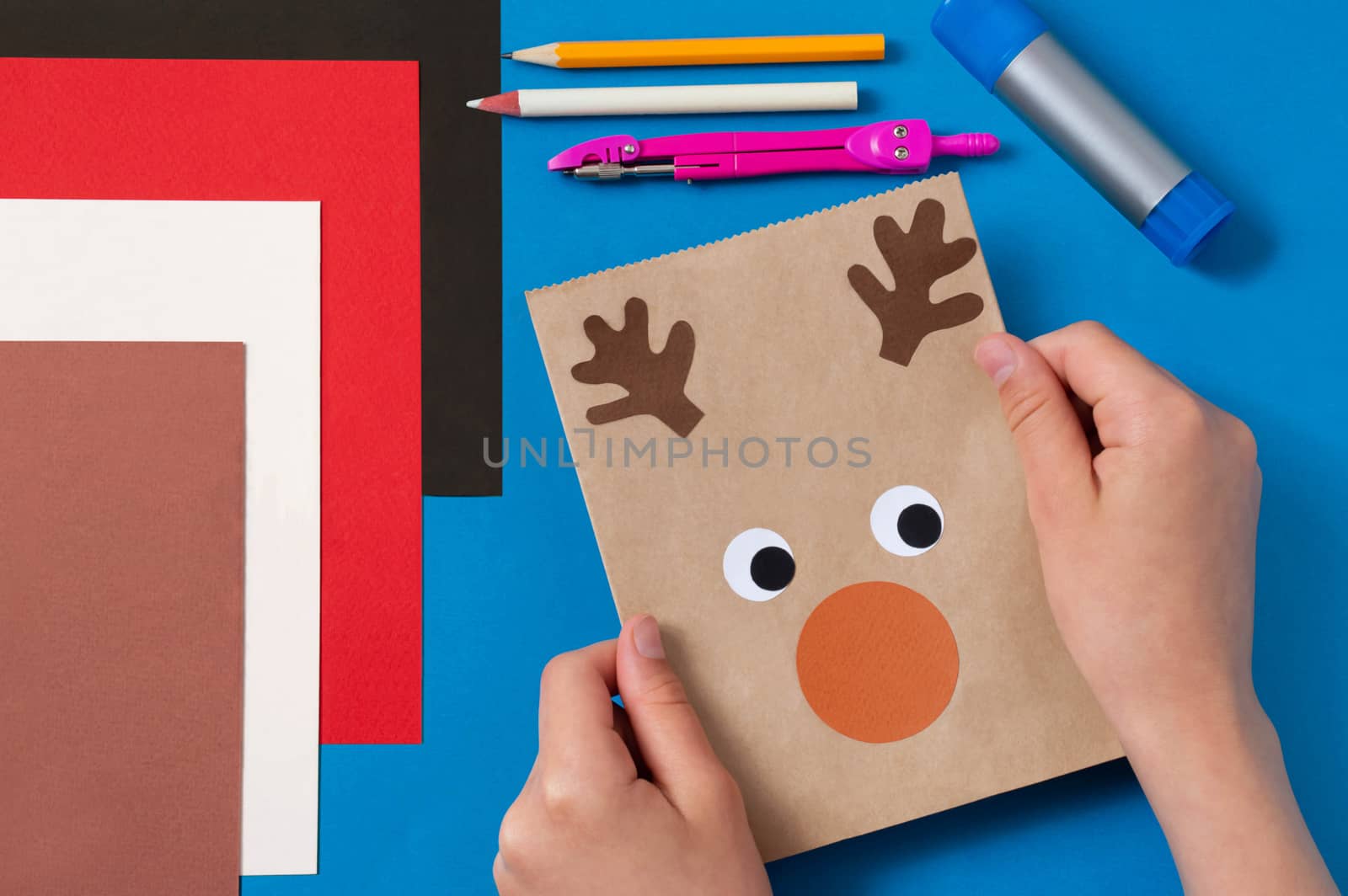 Child decorates craft gift bags for Christmas. Original project for children. DIY concept. Step-by-step photo instructions. Step 8. Glue details of deer's face