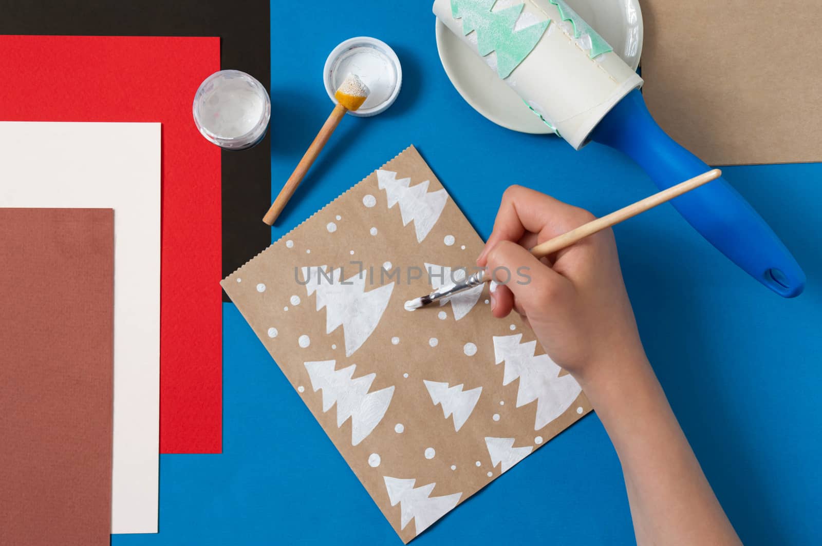 Child decorates craft gift bags for Christmas. Original project for children. DIY concept. Step-by-step photo instructions. Step 4. Paint snow 