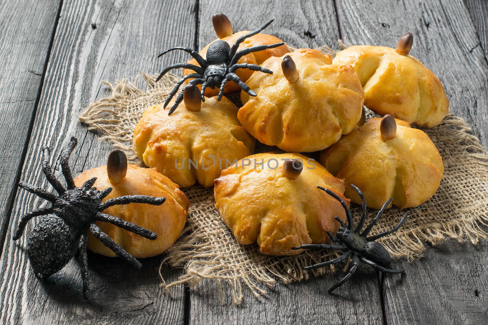 Homemade sweet pumpkin buns. Original baking in form of pumpkin and black toy spiders. Symbols Halloween. Idea of design meal for Halloween party. Scary and funny Halloween food