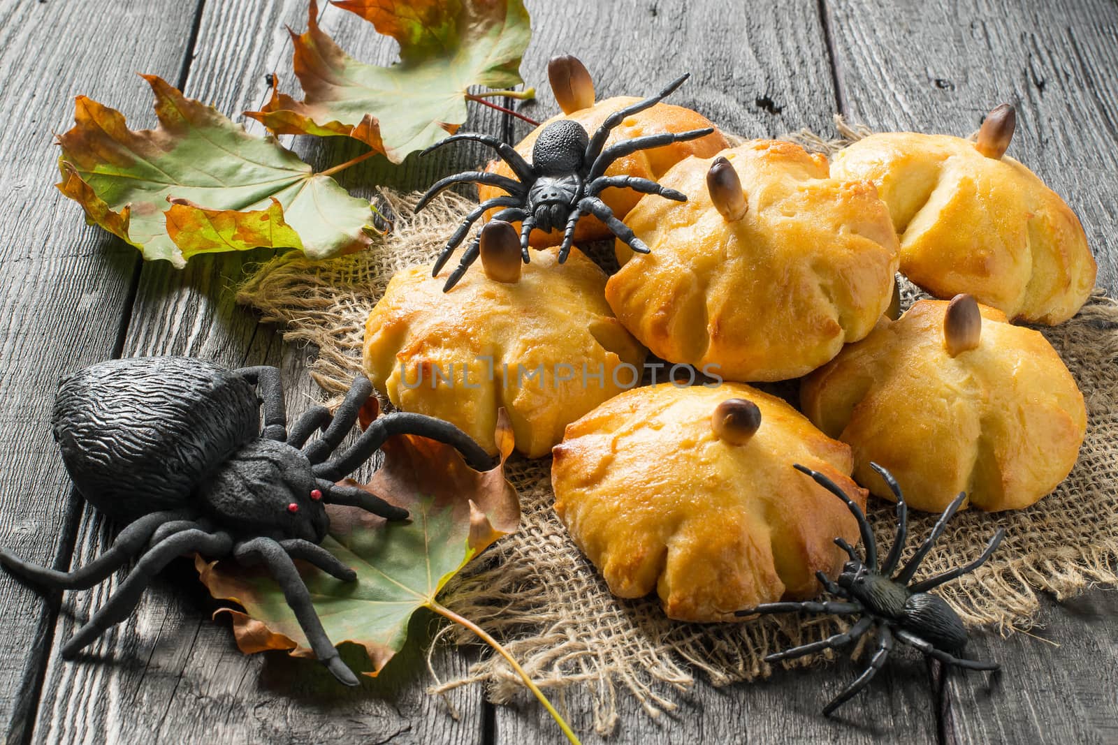 Homemade sweet pumpkin buns. Original baking in form of pumpkin and black toy spiders. Symbols Halloween. Idea of design meal for Halloween party. Scary and funny Halloween food 