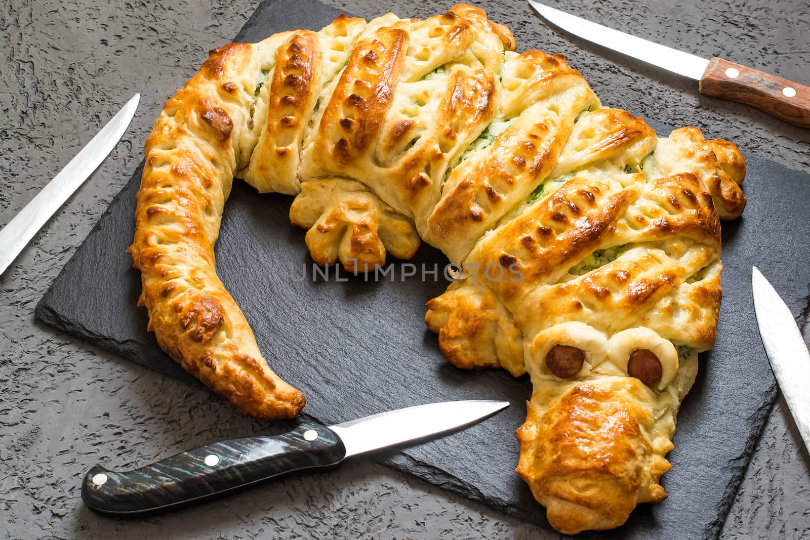 Original cake in form of crocodile with potatoes, cheese and herbs and knives. Cake is served to Halloween party as fun and spooky monster