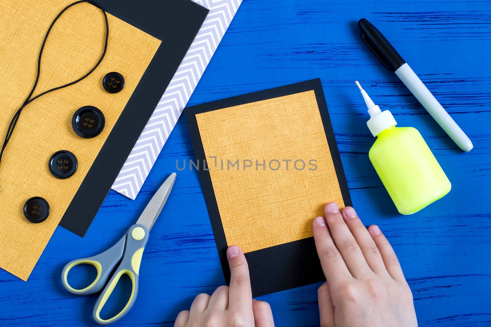 Child makes card with spiders to Halloween. Children's art project. DIY concept. Step-by-step photo instruction. Step 2. Glue yellow paper onto black cardboard card