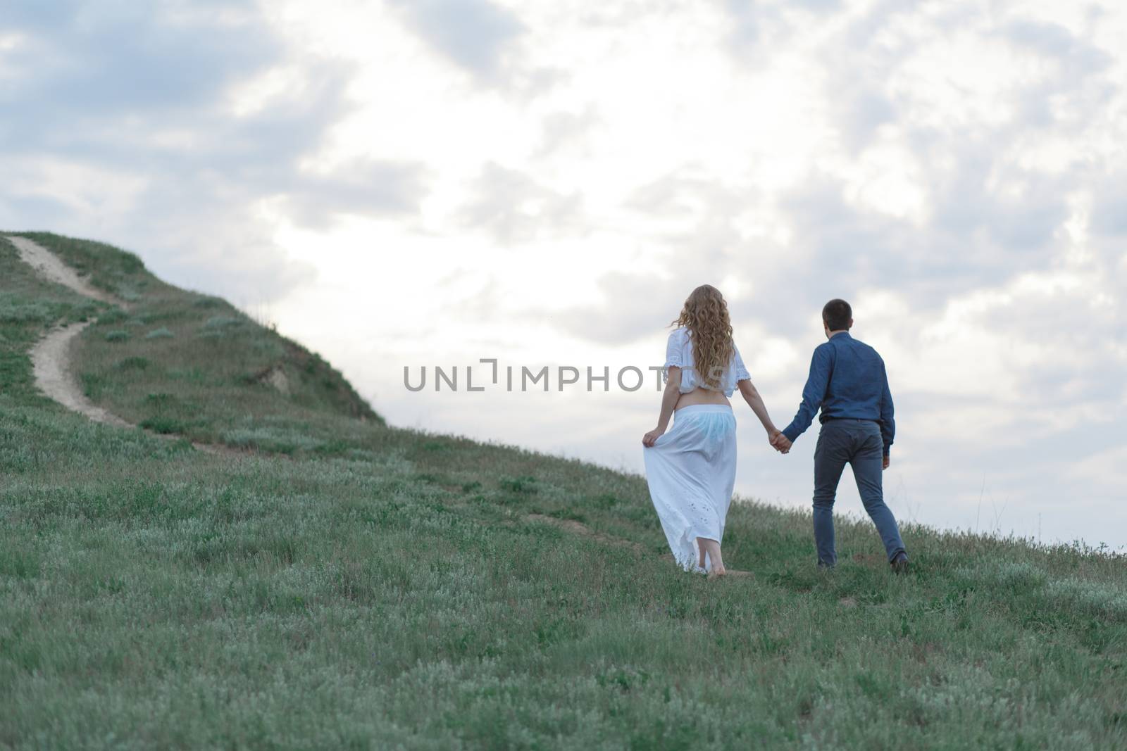 A couple in love, a pregnant wife in a white outfit are walking in a hilly field. Overcast weather,
