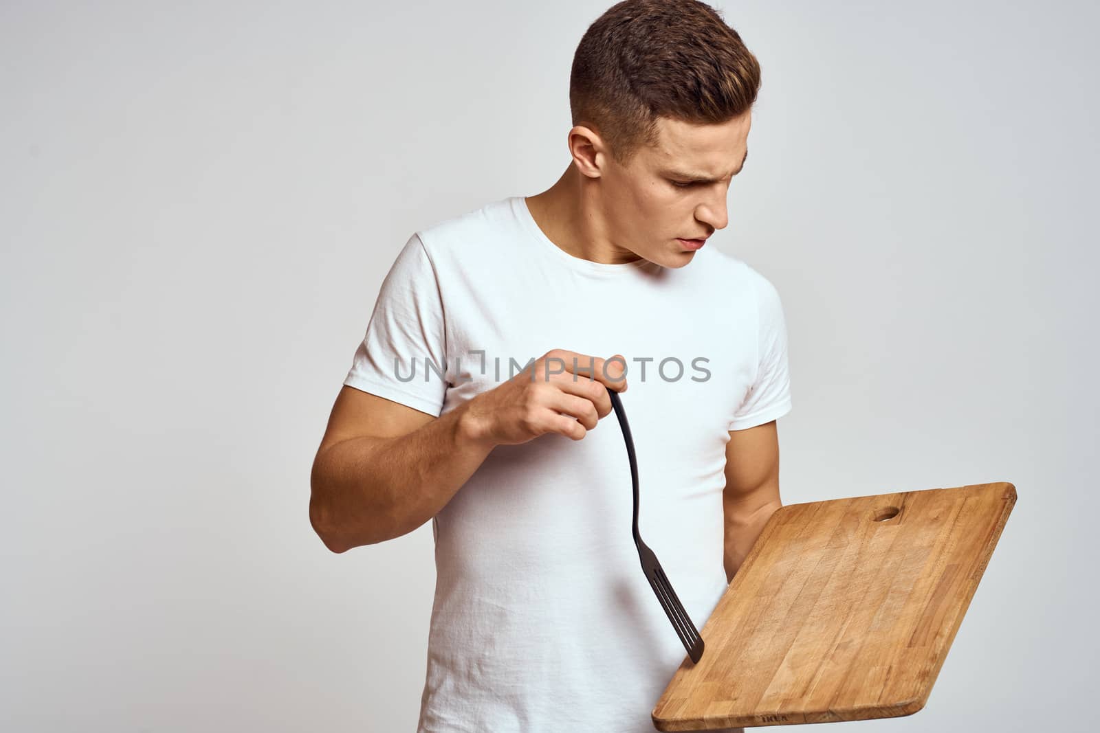 Guy with kitchen tools in hands on a light background cropped view of emotions fun model. High quality photo