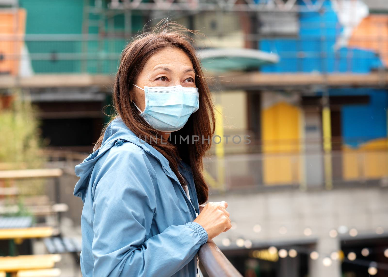 Asian woman in a face mask and a blue coat walking around Europe by Iryna_Melnyk