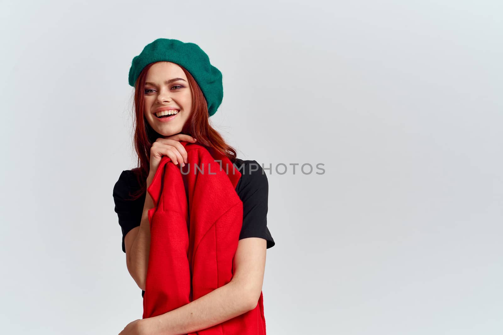 A woman holds in her hand a red coat and a dark T-shirt Green hat cropped view of a light background by SHOTPRIME