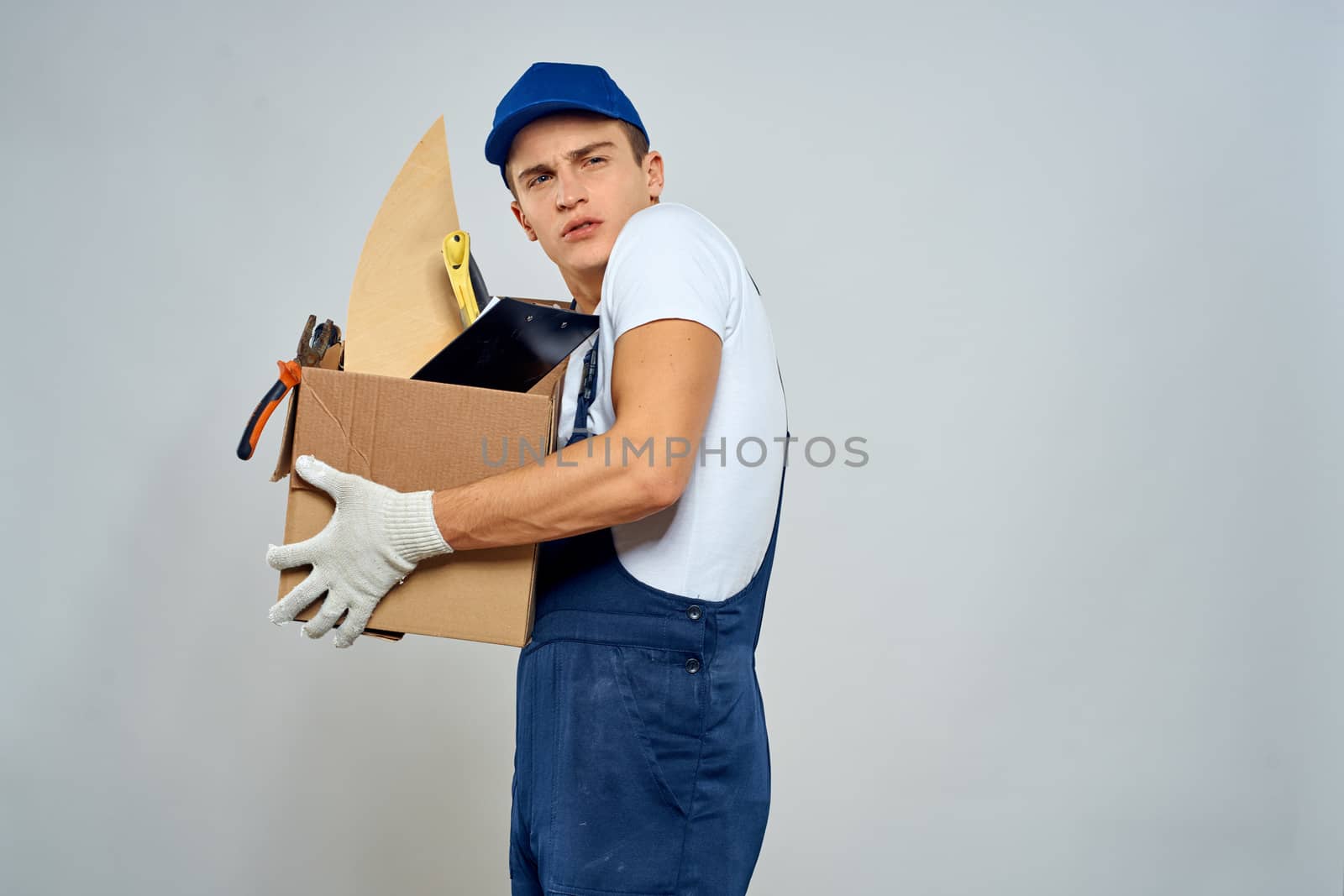 man in working uniform with a box in his hands tools loader delivery light background. High quality photo