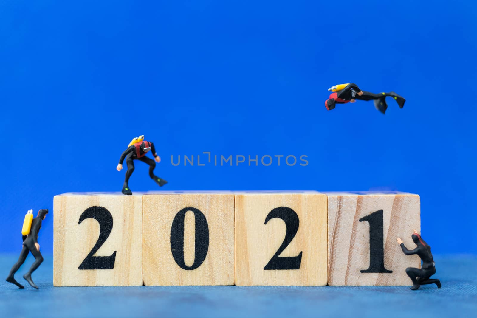 Miniature people divers diving around wooden block 2021 , Happy new Year concept