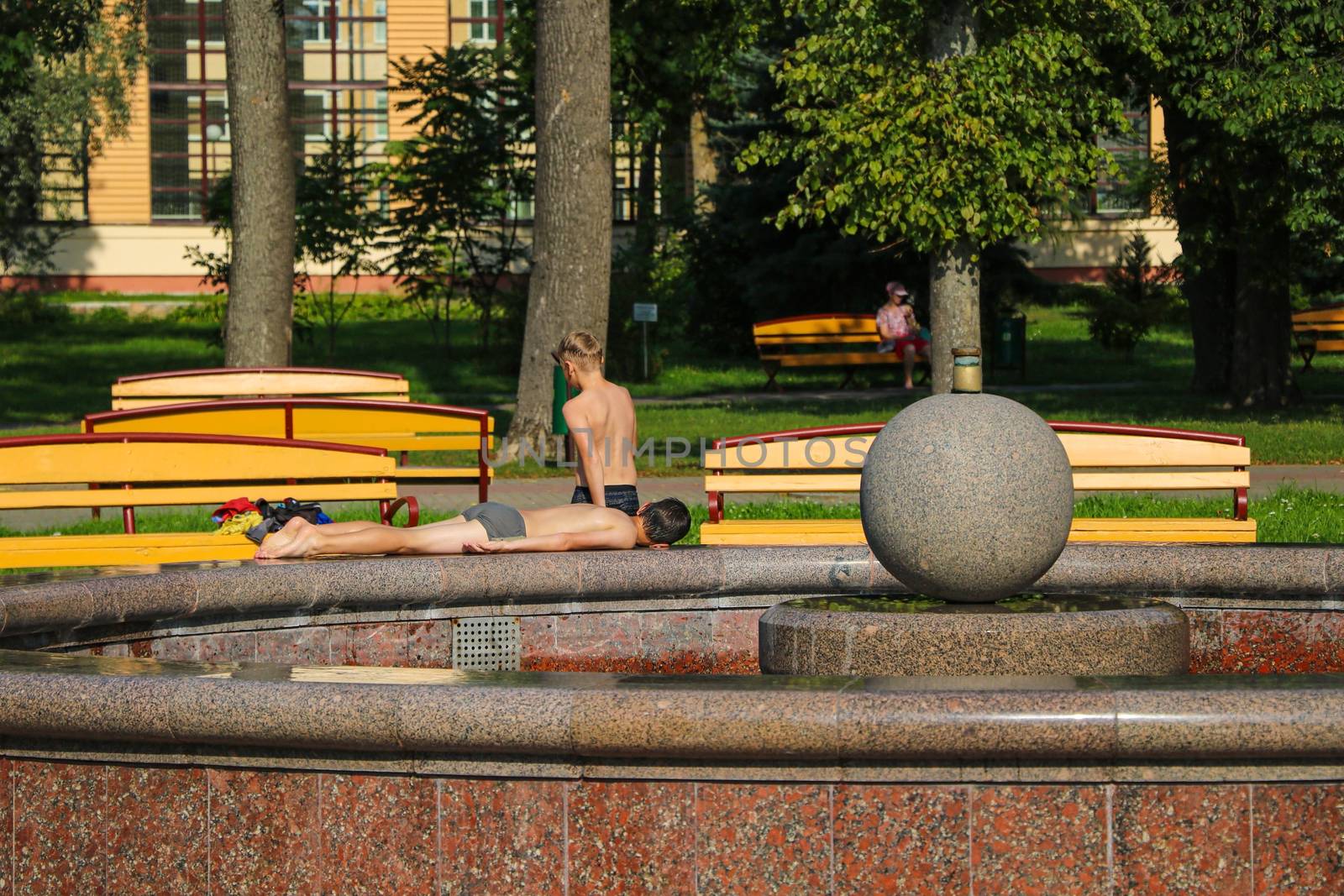 Children sunbathe in the sun near the fountain on a clear day by kip02kas
