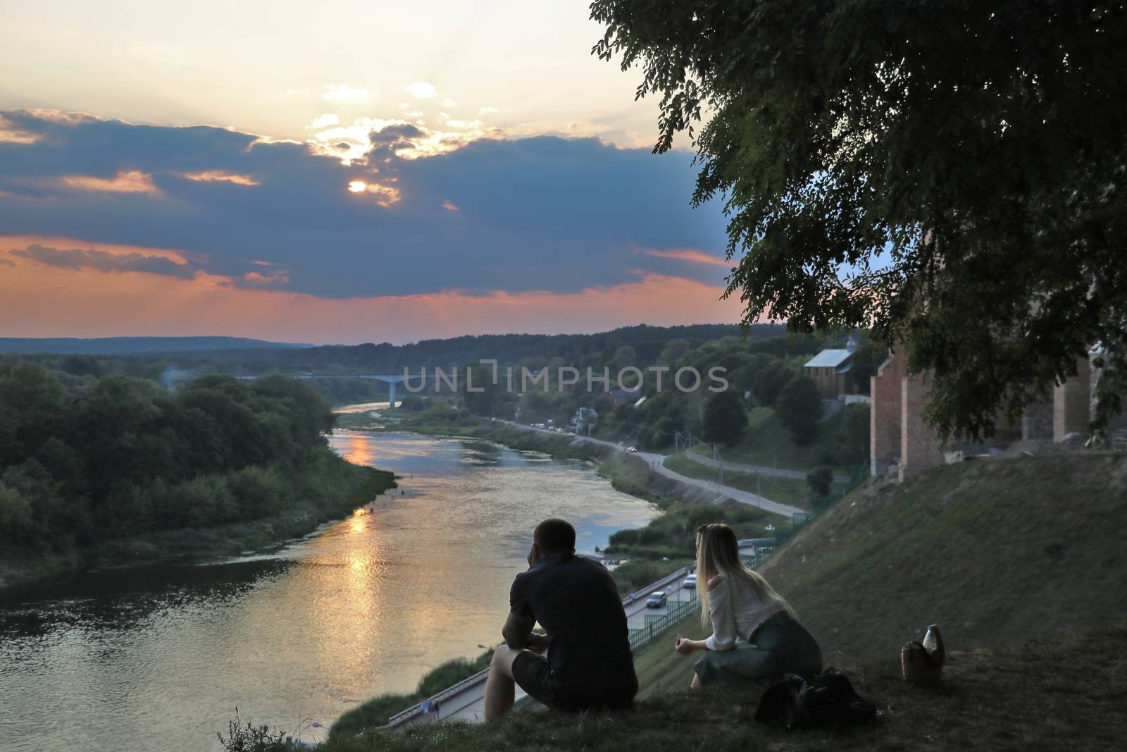 A young couple sits on the grass and watches the sunset
