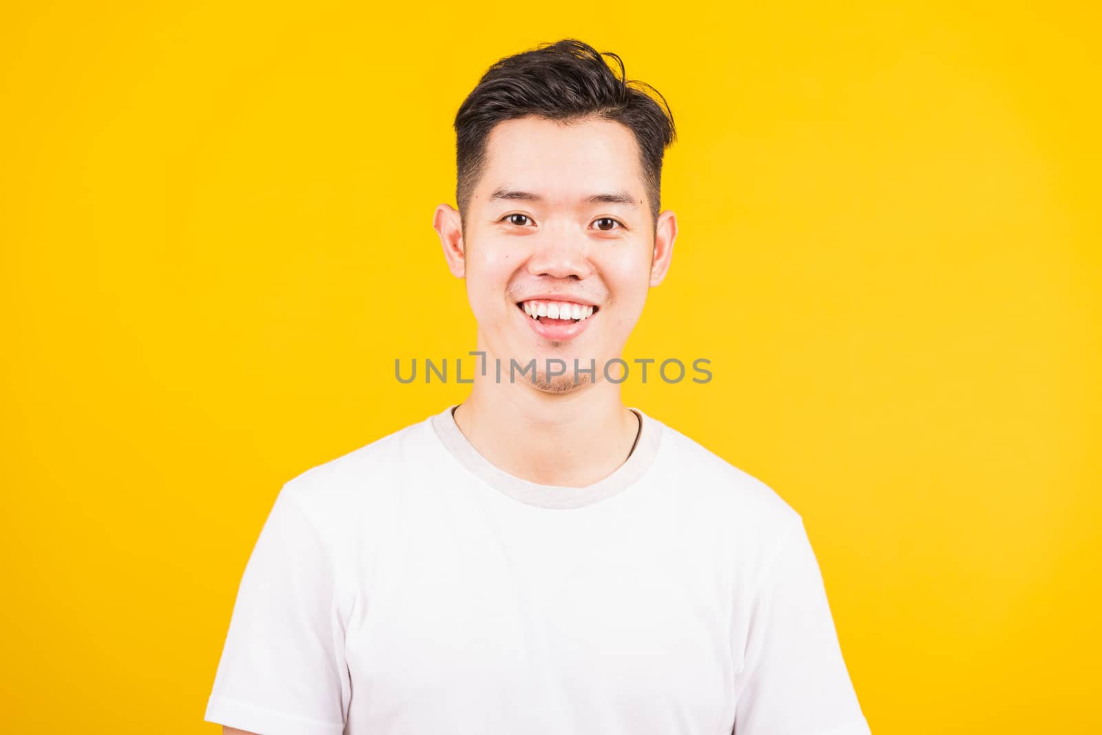 Close up portrait happy Asian handsome young man smiling standing wearing white t-shirt looking to camera, studio shot isolated yellow background