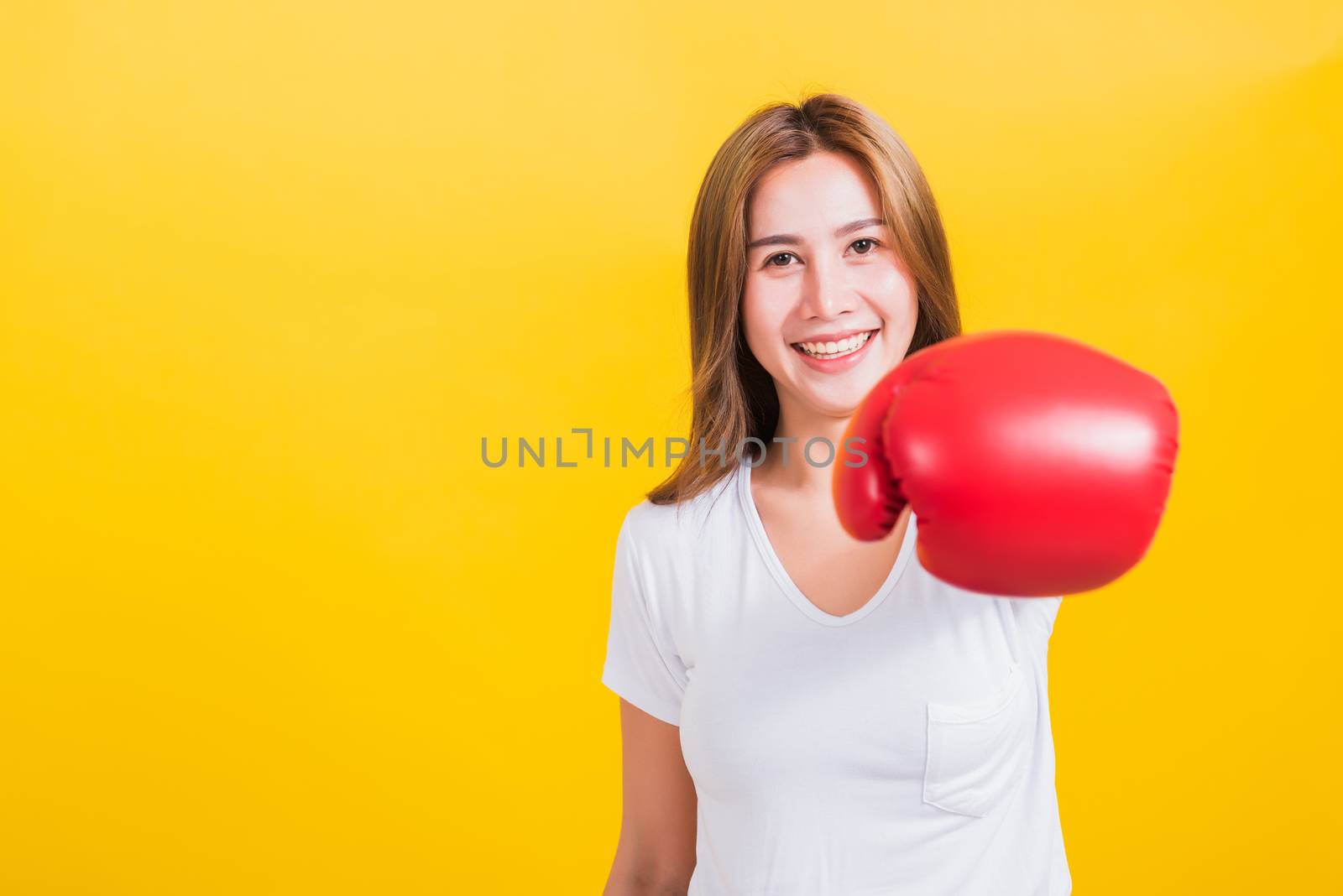 Portrait Asian Thai beautiful young woman standing smile wearing red boxing gloves and punch to the front camera, studio shot isolated on yellow background, There was copy space for text