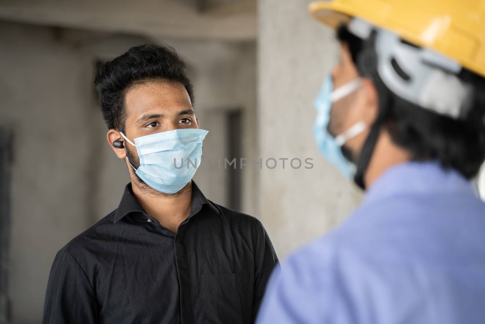 Shoulder shot, Construction worker and engineer at site talking by wearing medical mask with social distance - concept of business, industry reopen and covid-19 safety measures at workplace. by lakshmiprasad.maski@gmai.com