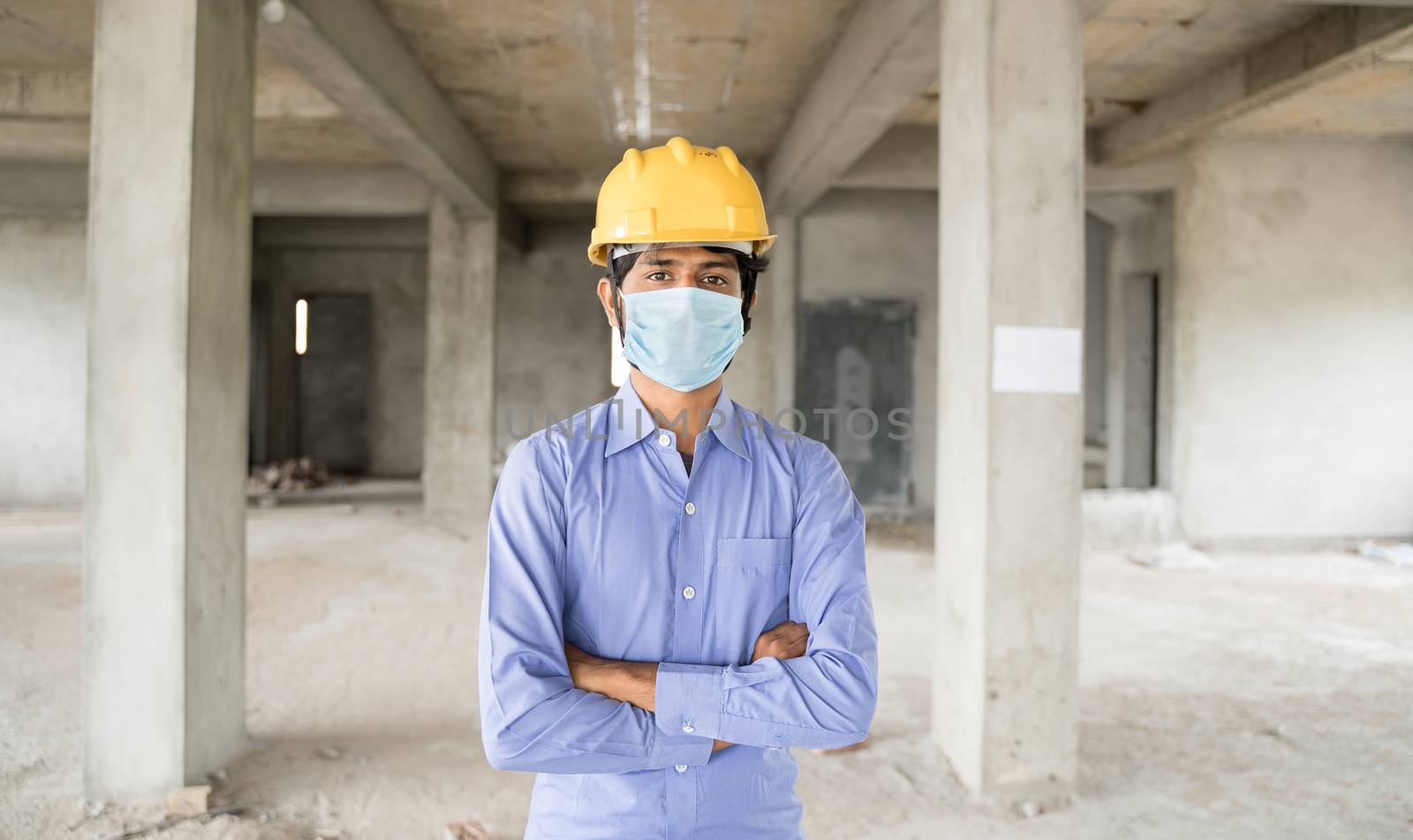 Concept of back to work, opening of construction sites after covid-19 pandemic - portrait of confident construction worker in a construction helmet arms crossed with medical mask at site. by lakshmiprasad.maski@gmai.com